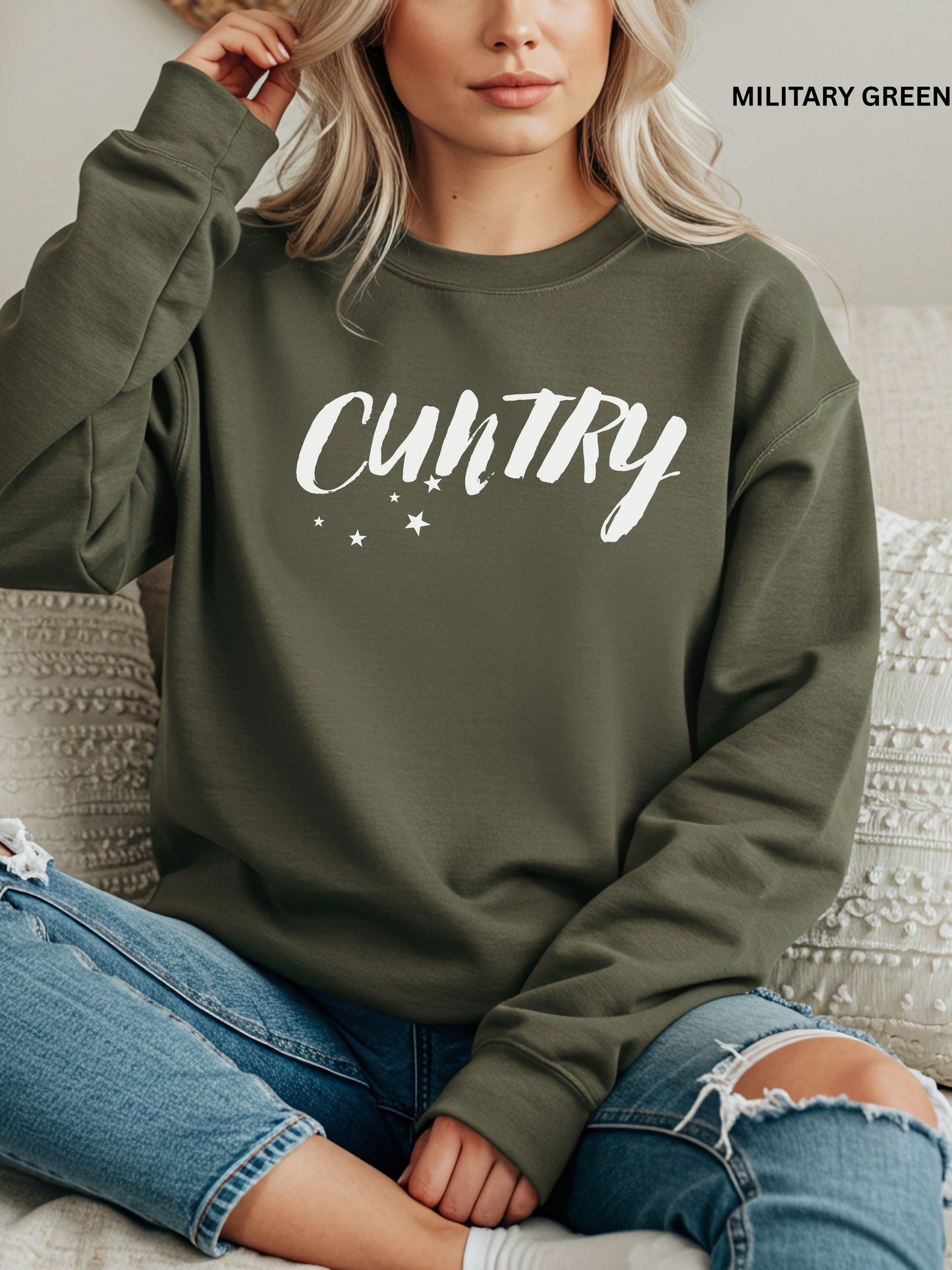Person wearing a military green  sweatshirt with 'CUNTRY' printed on it, sitting on a couch.