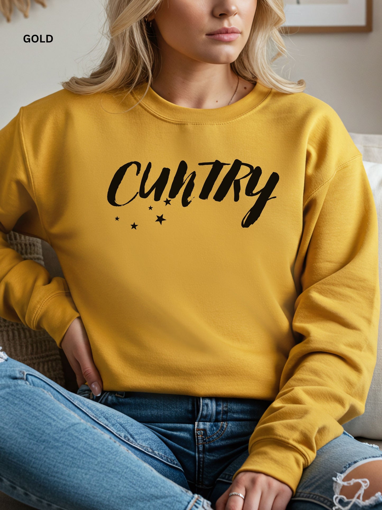 Person wearing a gold sweatshirt with 'CUNTRY' printed on it, sitting on a couch.