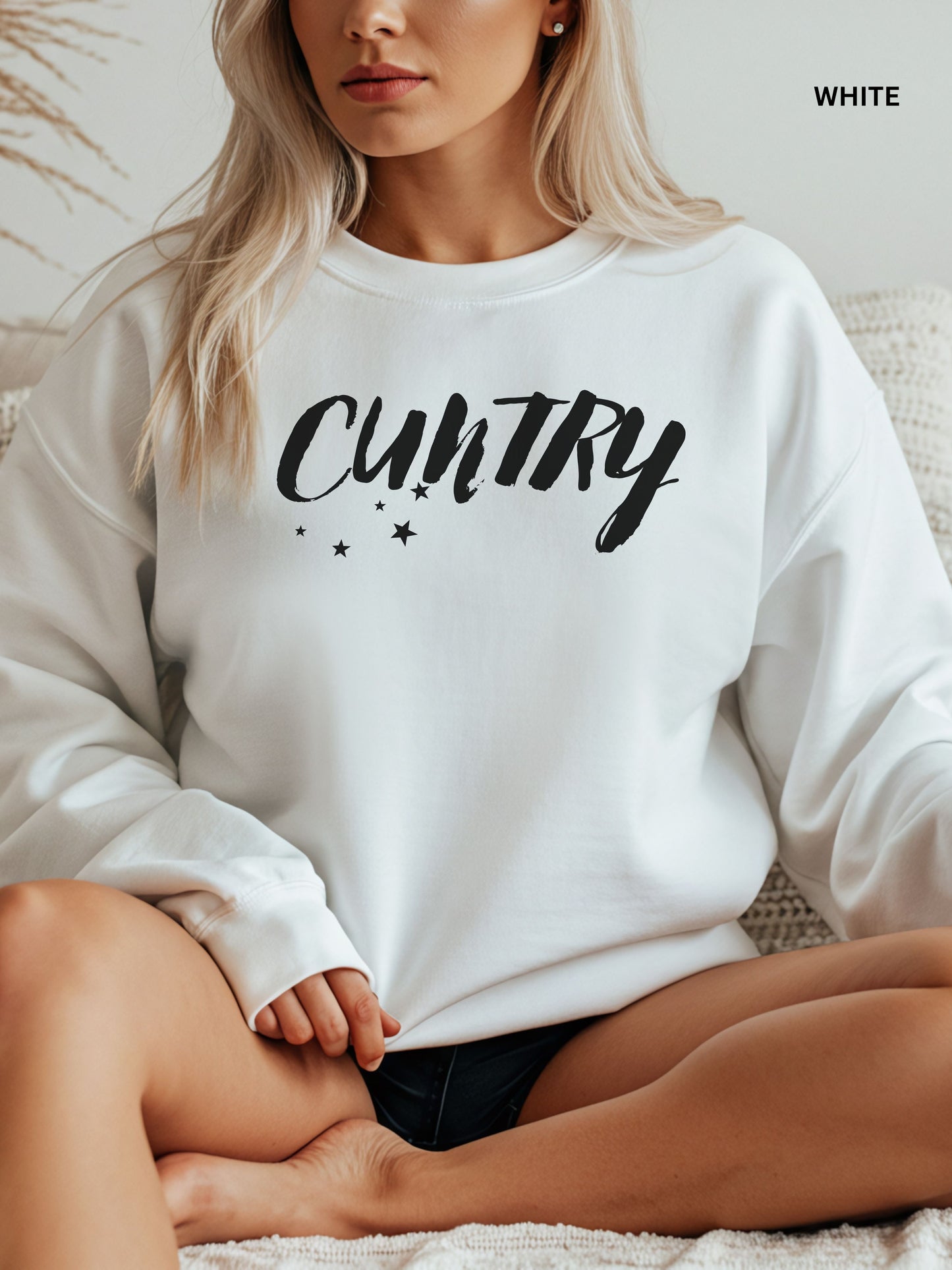 Person wearing a white sweatshirt with 'CUNTRY' printed on it, sitting on a couch.