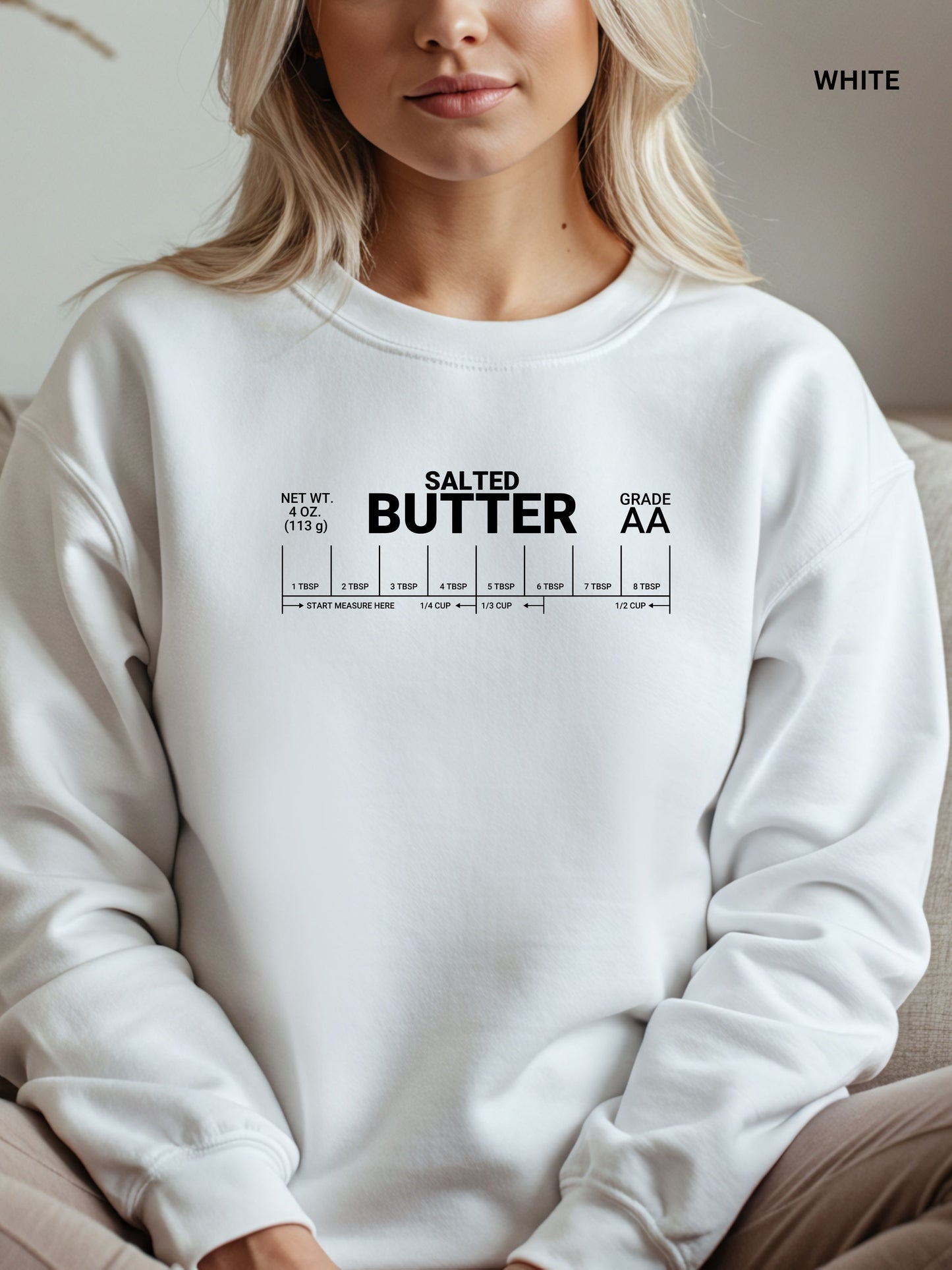 White sweatshirt with 'Salted Butter' text worn by a person, sitting on a couch.