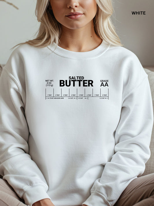 White sweatshirt with 'Salted Butter' text worn by a person, sitting on a couch.