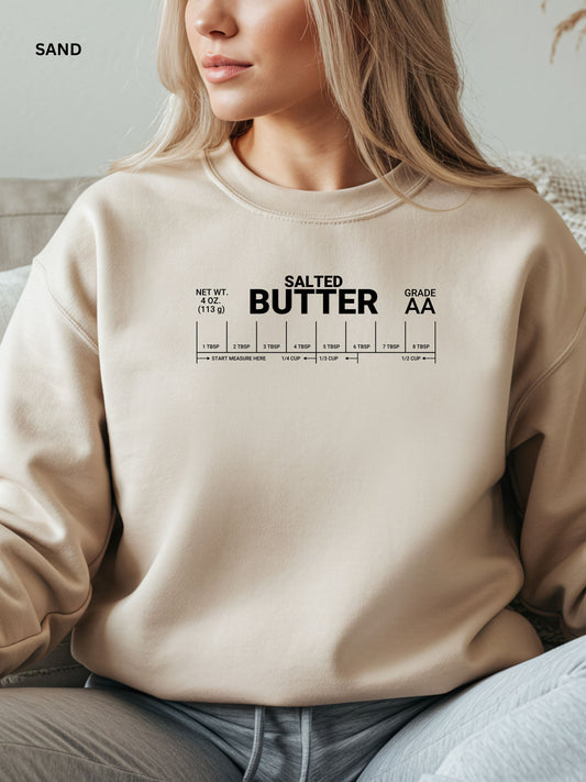 Person wearing a beige sweatshirt with 'Salted Butter' text design.