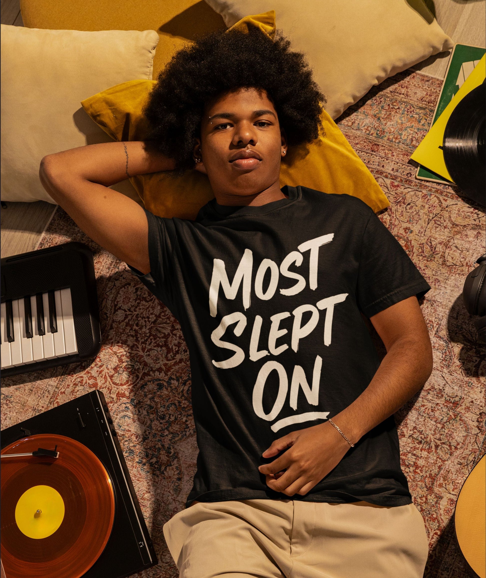 Person wearing a black t-shirt with 'MOST SLEPT ON' text, lying on a patterned floor.