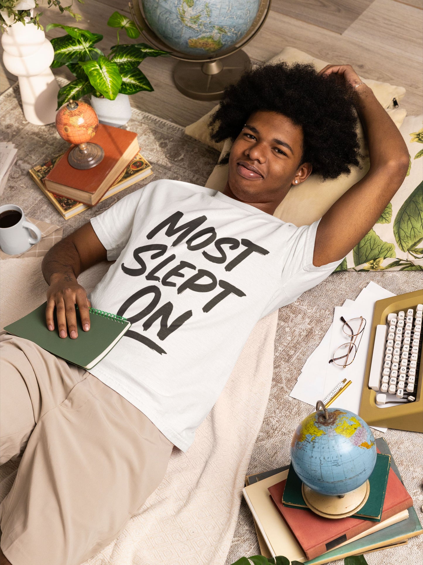 Person wearing a 'Most Slept On' t-shirt in a casual setting with books and a globe.