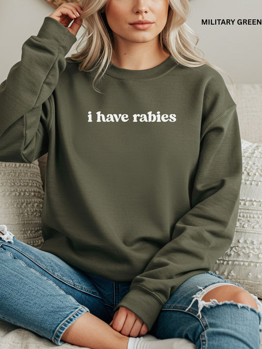Person wearing a military green sweatshirt with 'i have rabies' text, sitting on a couch.