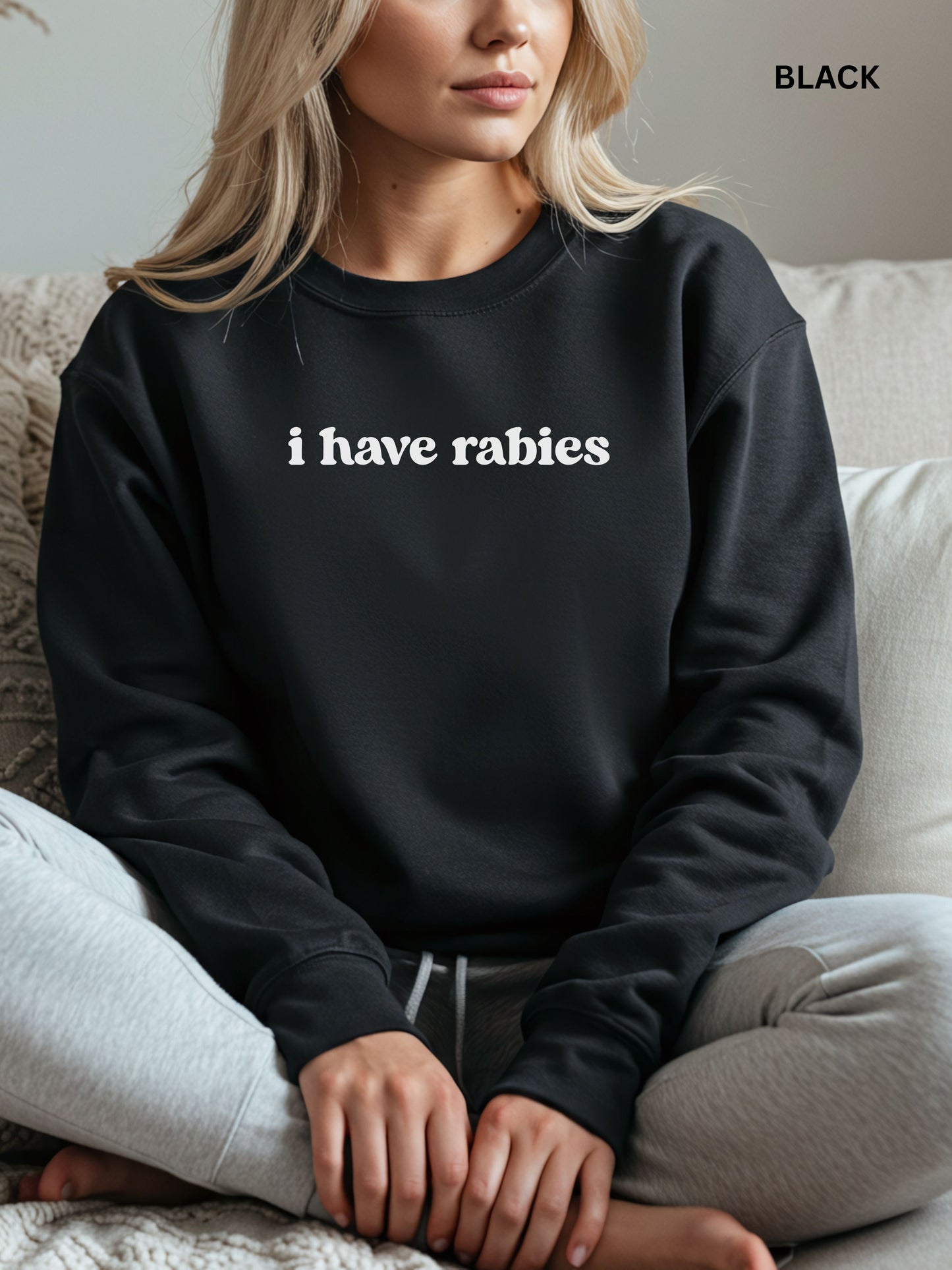 Person wearing a black sweatshirt with 'i have rabies' text, sitting on a couch.