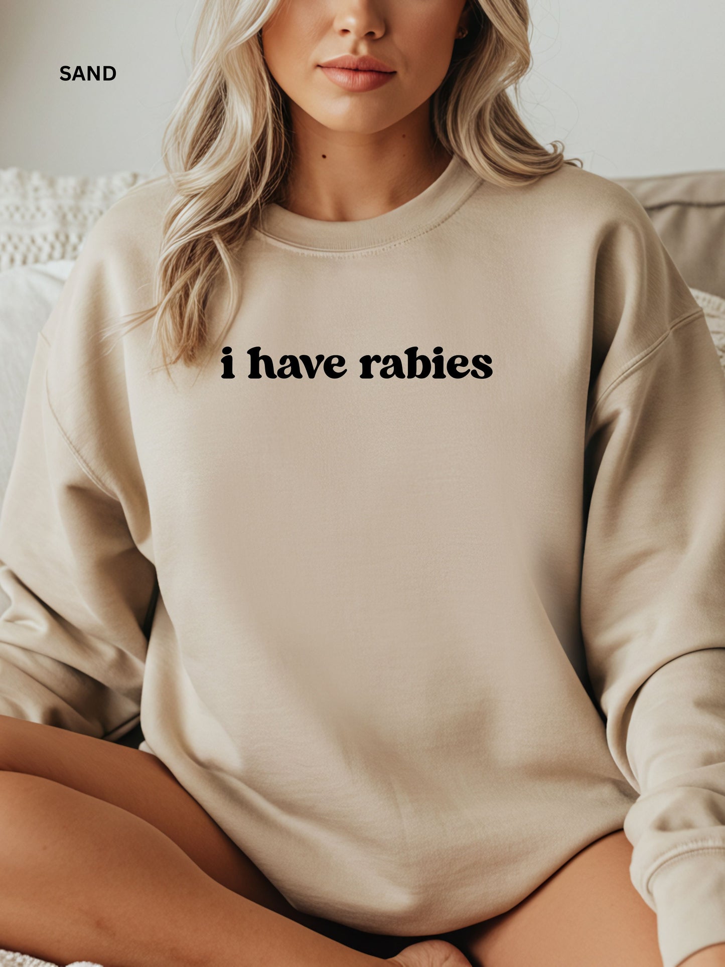 Person wearing a sand sweatshirt with 'i have rabies' text, sitting on a couch.