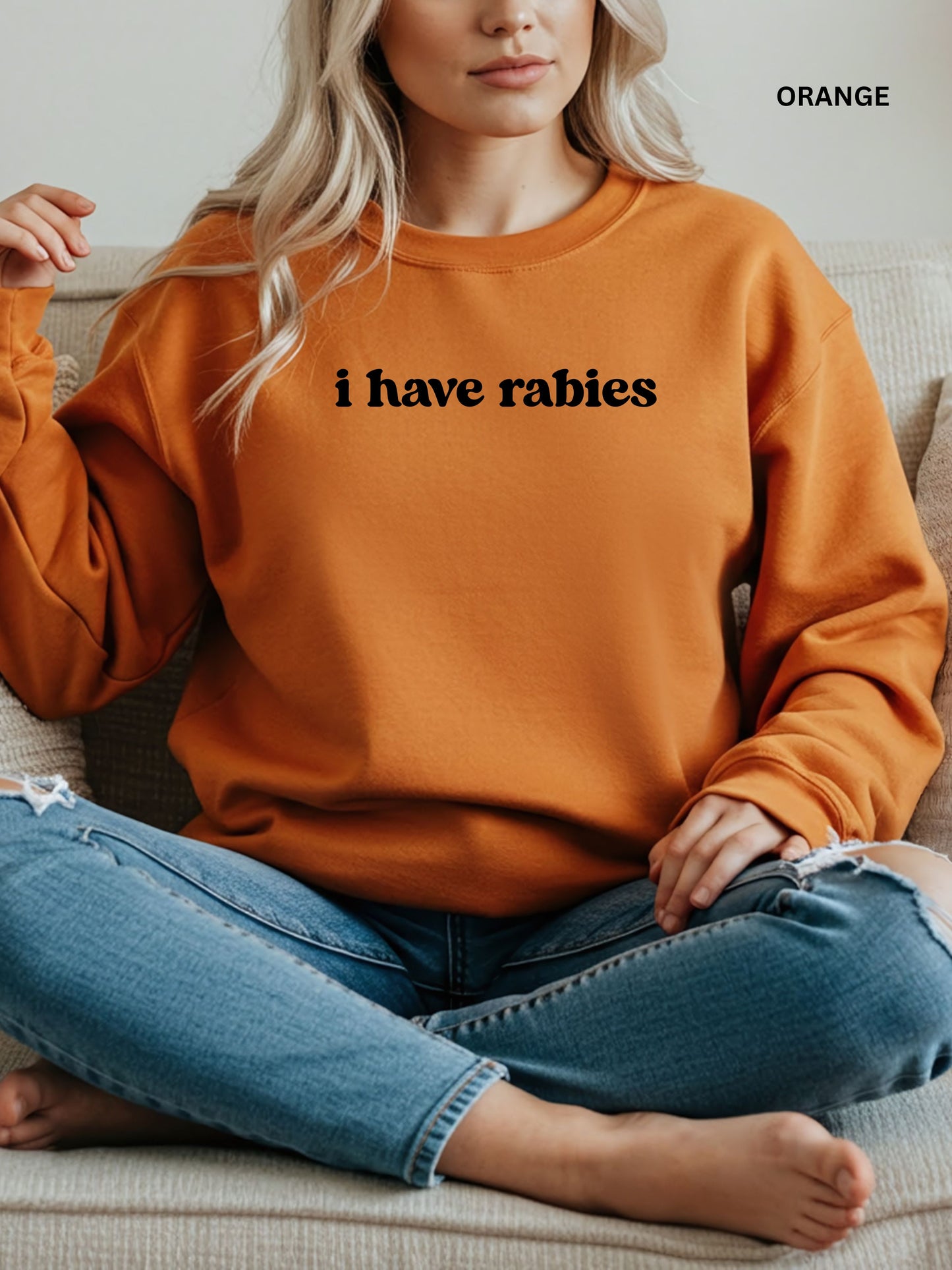 Person wearing an orange sweatshirt with 'i have rabies' text, sitting on a couch.