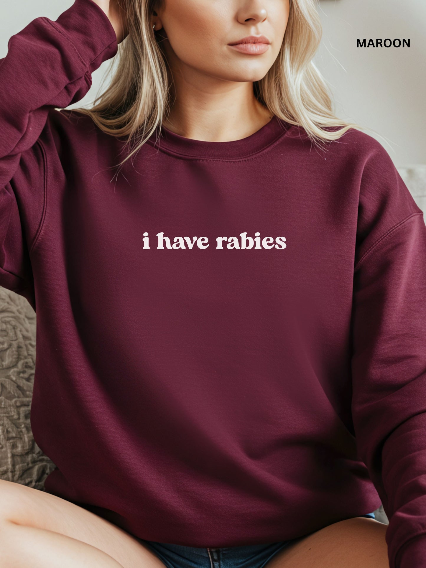 Person wearing a maroon sweatshirt with 'i have rabies' text, sitting on a couch.