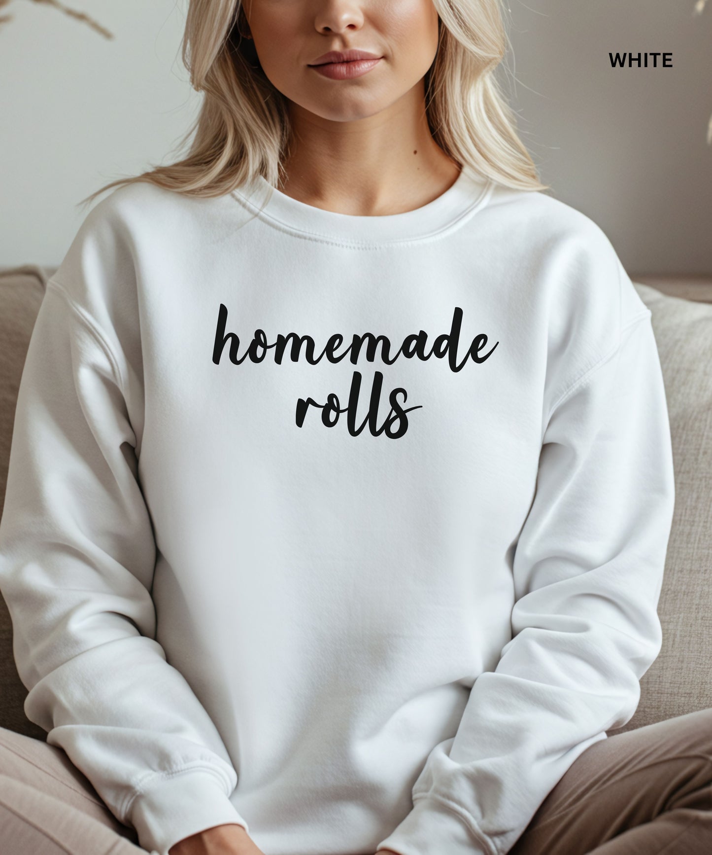 White sweatshirt with 'homemade rolls' text worn by a person, sitting on a couch.