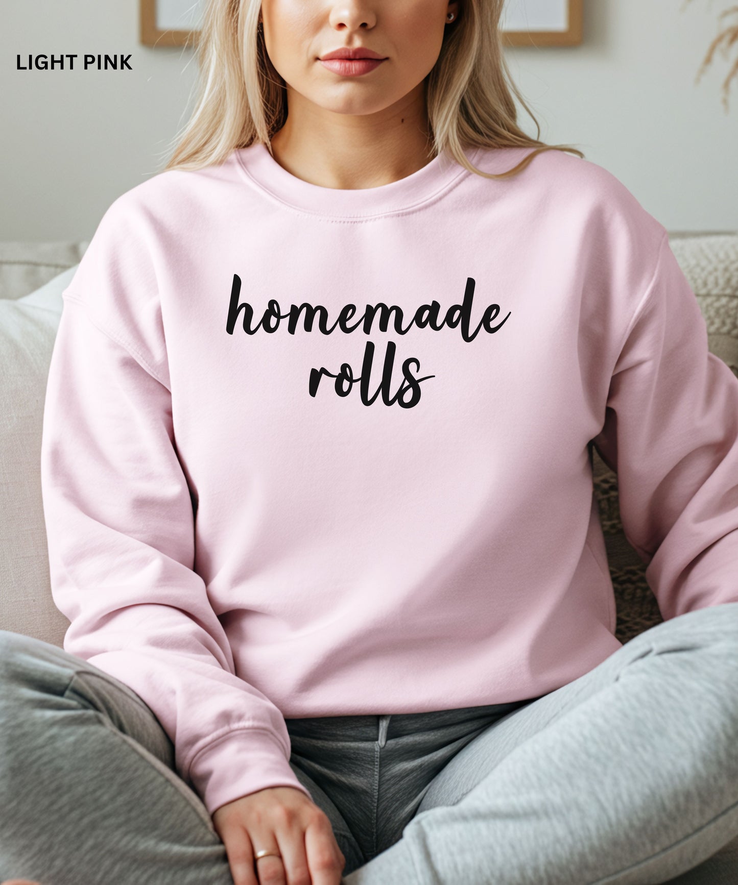 Person wearing a light pink sweatshirt with 'homemade rolls' text, sitting on a couch.