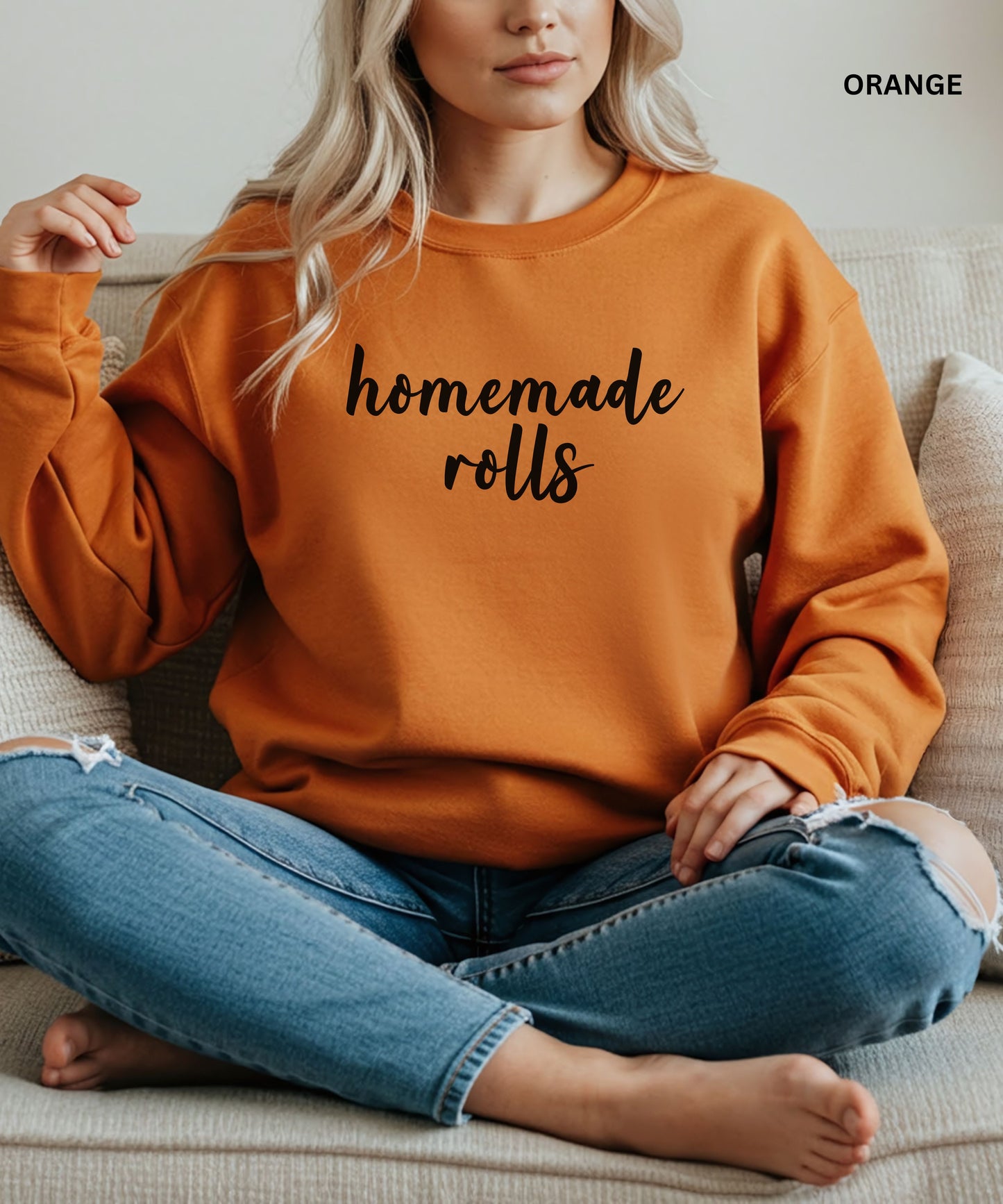 Person wearing an orange sweatshirt with 'homemade rolls' text, sitting on a couch.