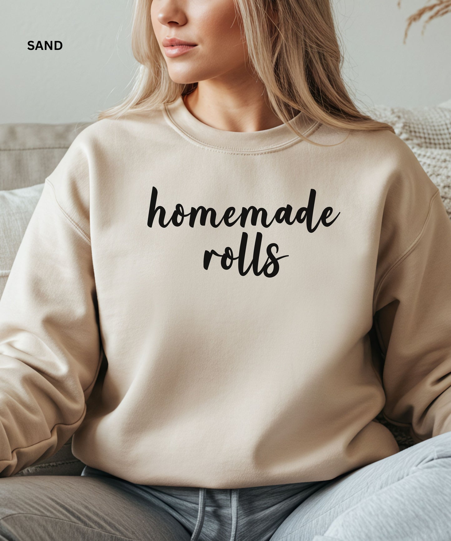 Person wearing a sand sweatshirt with 'homemade rolls' text, sitting on a couch.