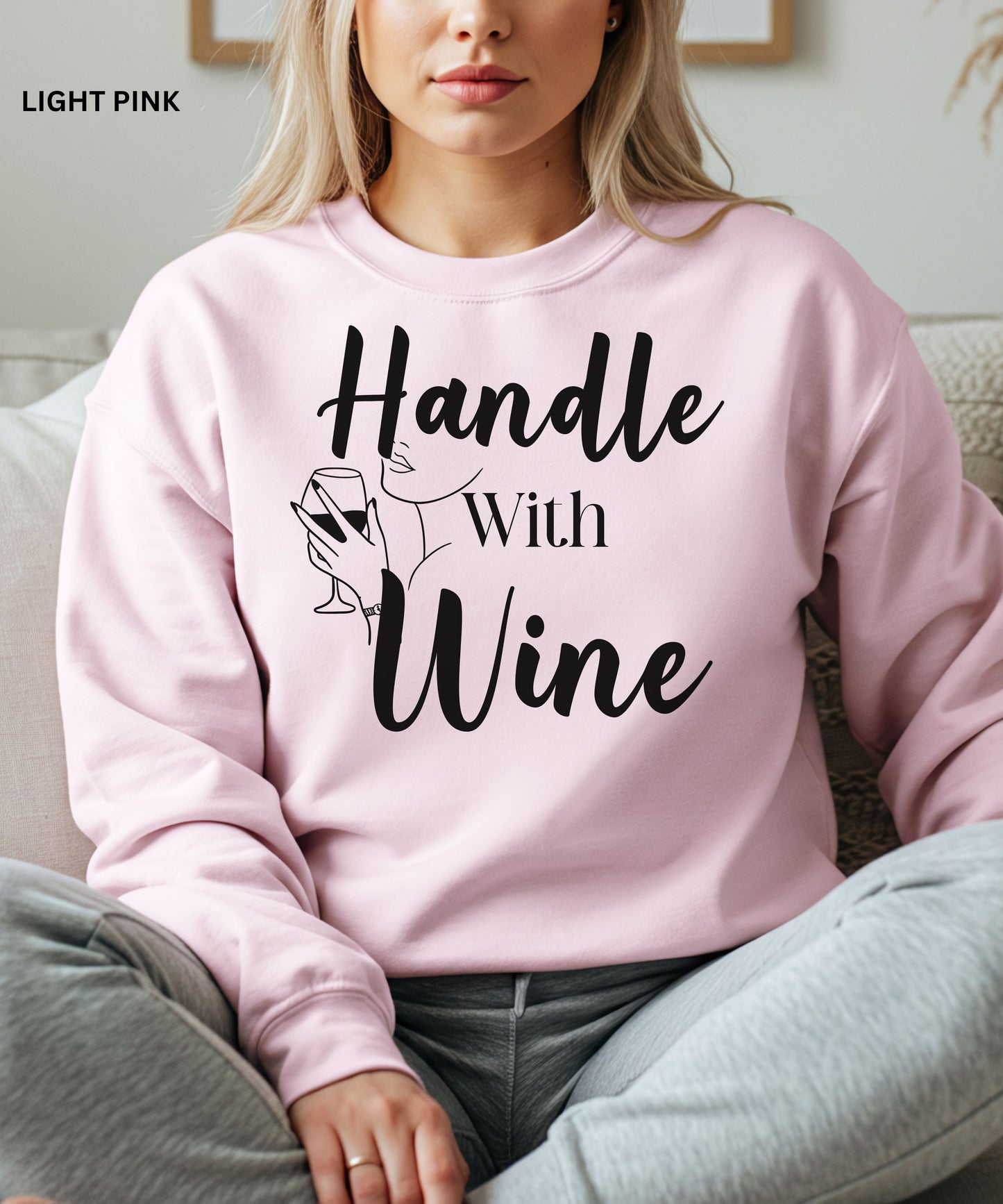 Person wearing a light pink sweatshirt with 'Handle With Wine' text and graphic.