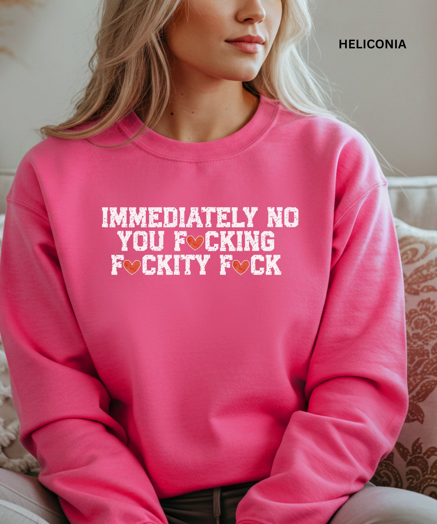 Person wearing a pink sweatshirt with text, sitting on a patterned couch.
