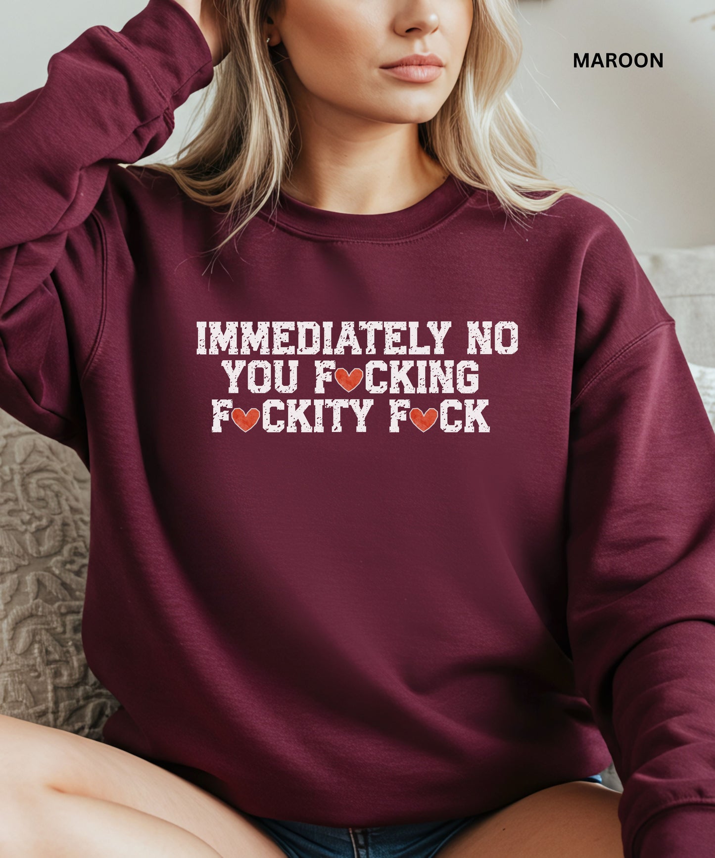 Maroon sweatshirt with graphic text worn by a person, sitting on a couch.