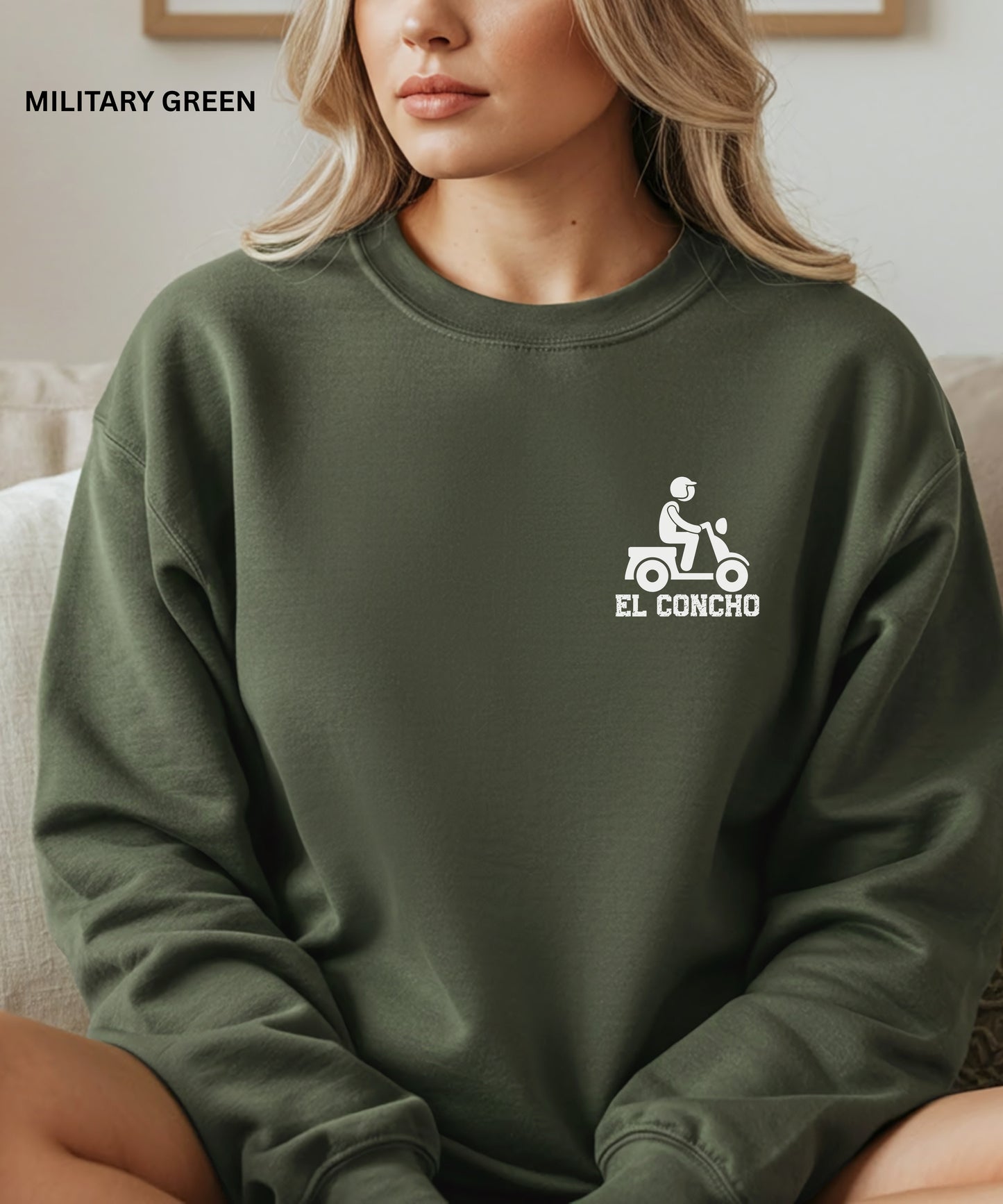 Person wearing a military green sweatshirt with a logo and text that says" el concho", sitting on a couch.