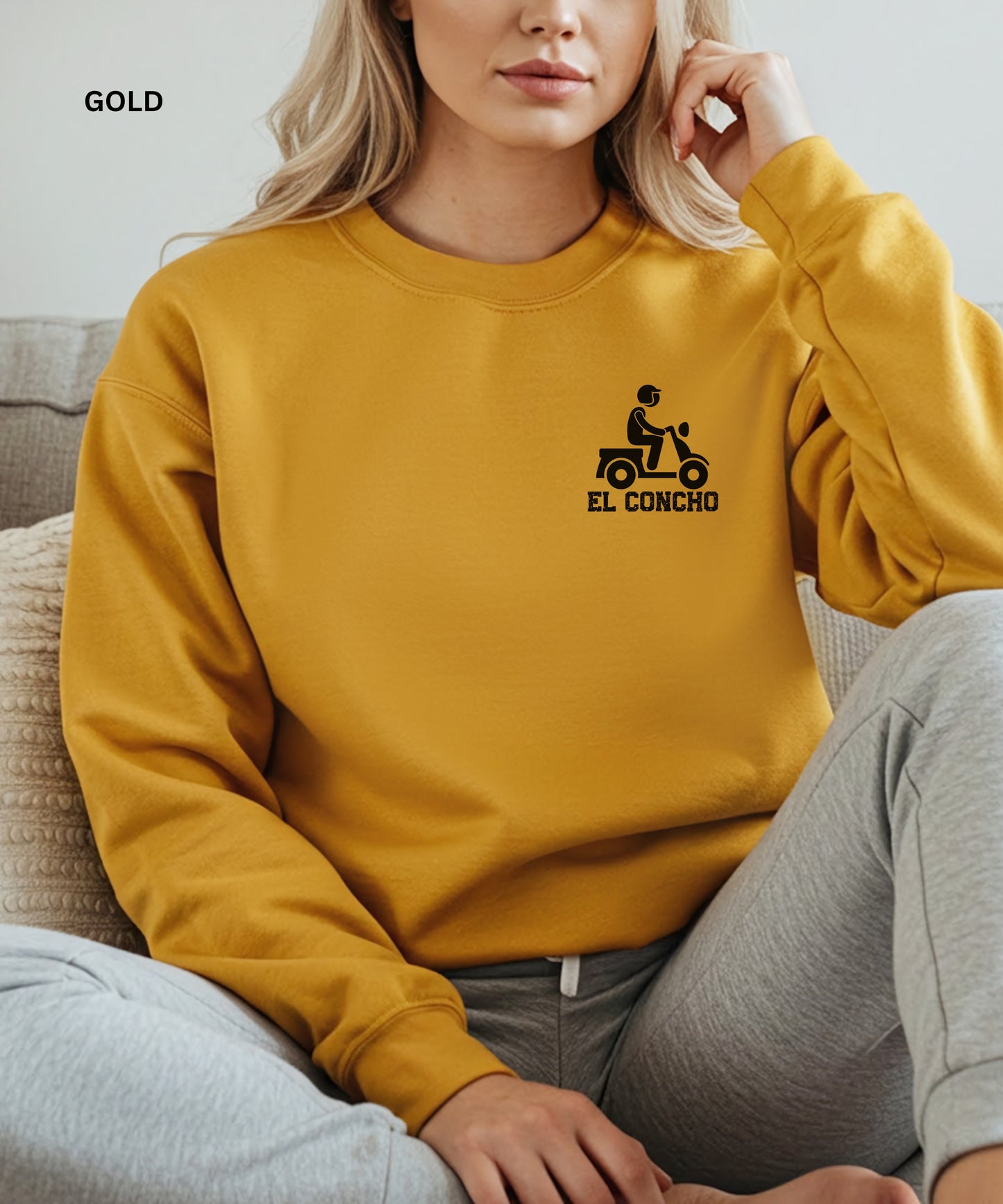 Person wearing a gold sweatshirt with a logo and text that says" el concho", sitting on a couch.