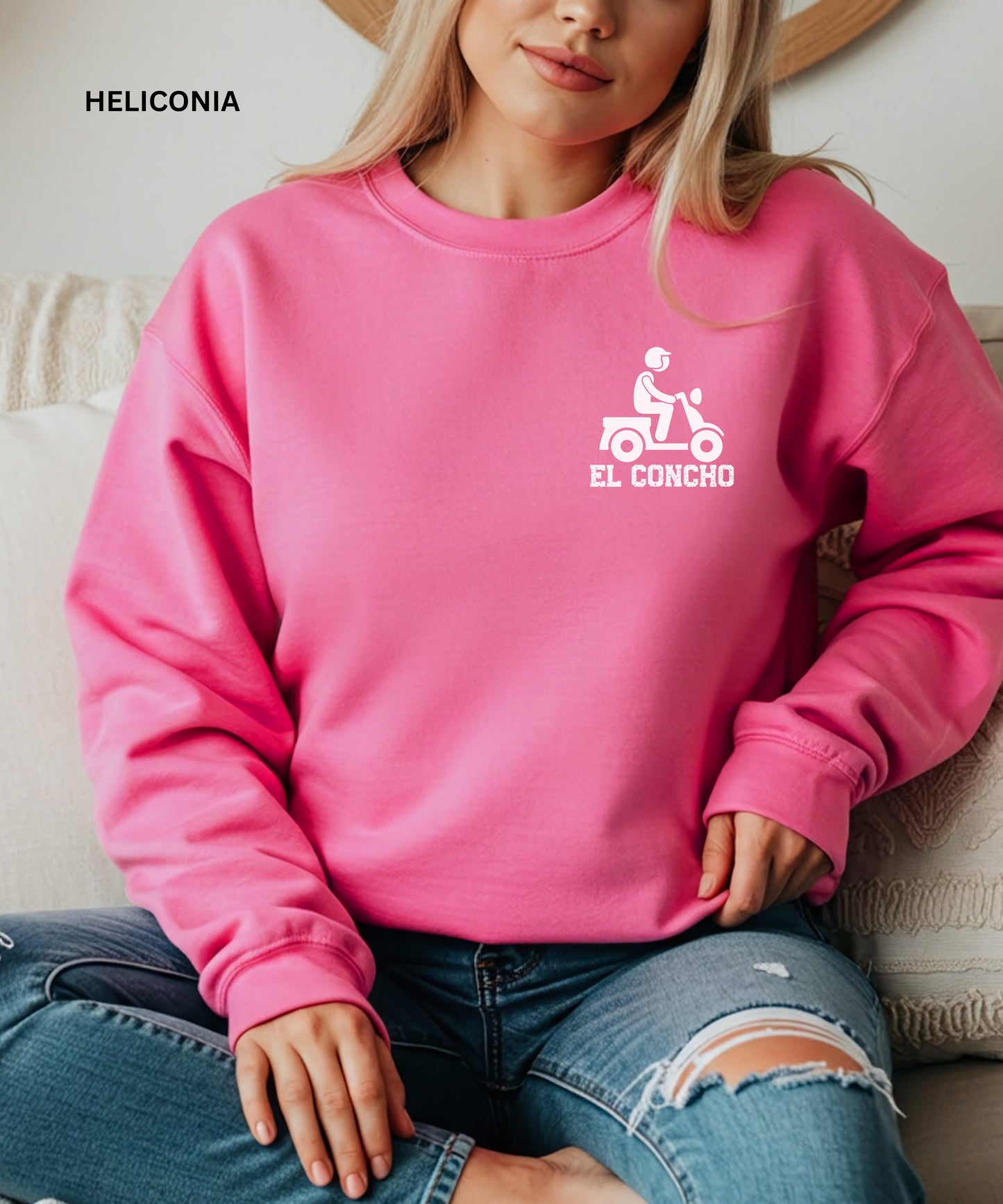 Person wearing a heliconia sweatshirt with a logo and text that says" el concho", sitting on a couch.