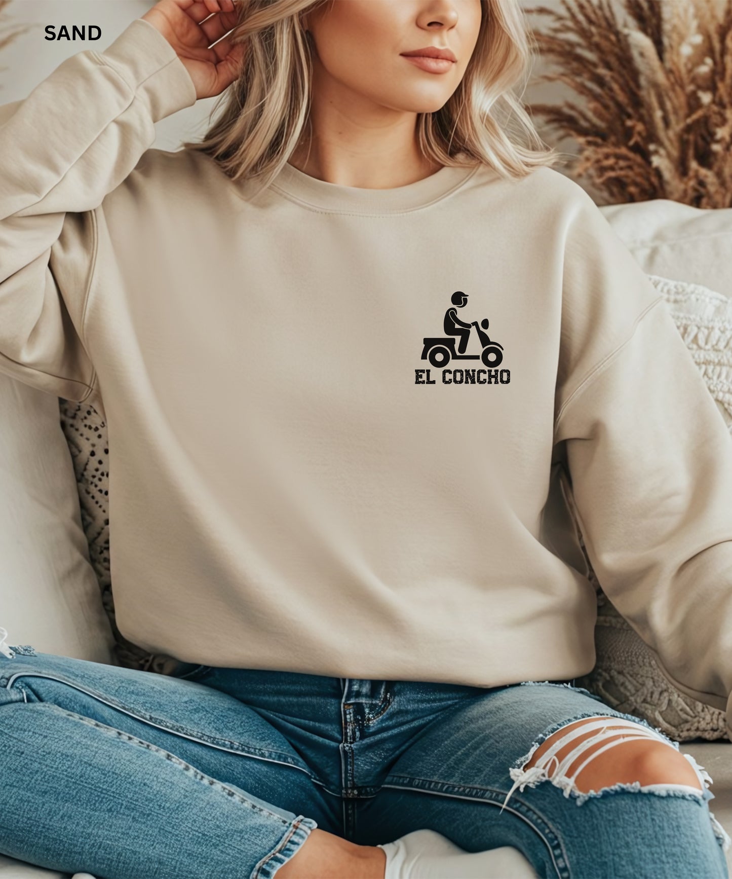 Person wearing a sand sweatshirt with a logo and text that says" el concho", sitting on a couch.