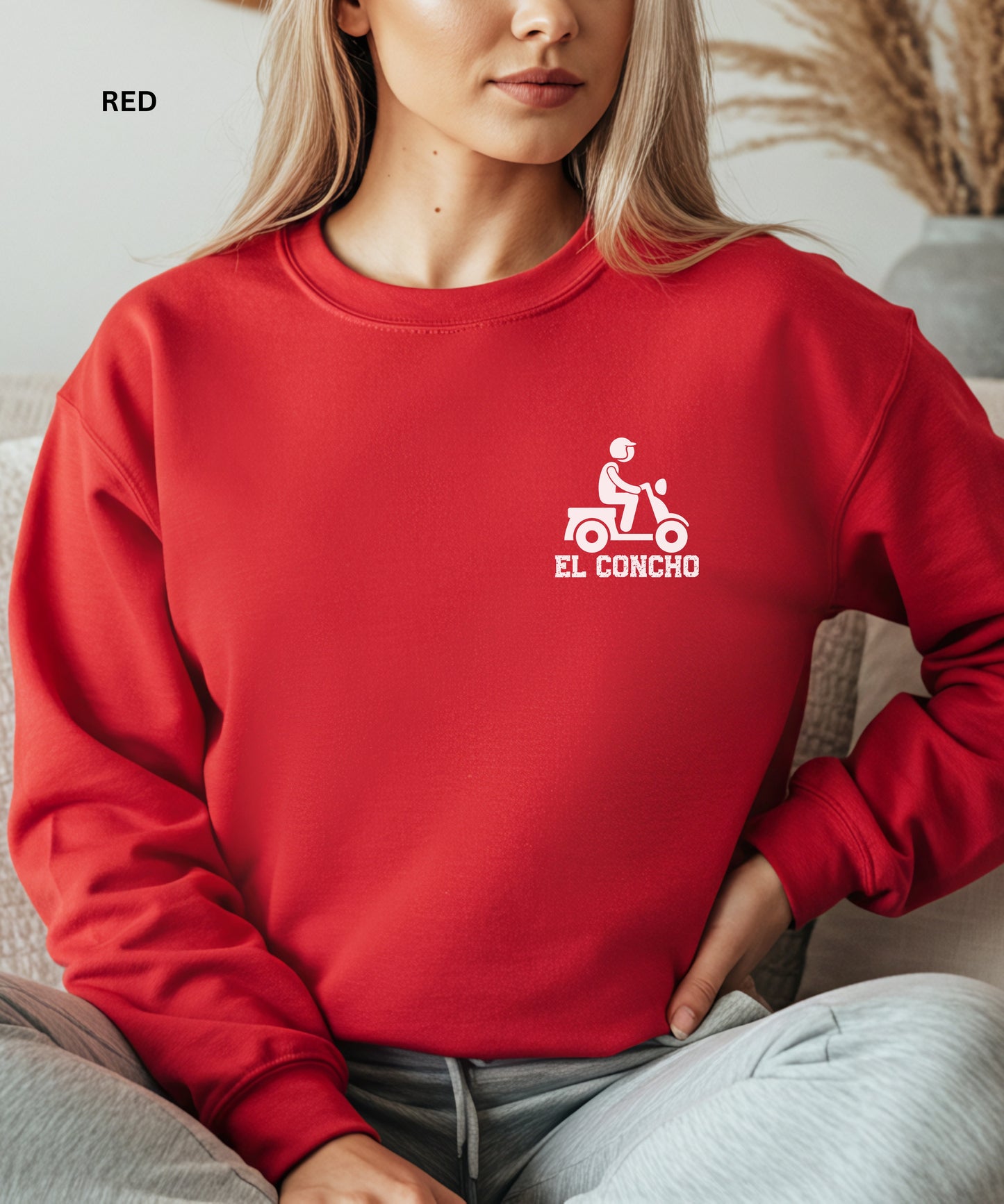 Person wearing a red sweatshirt with a logo and text that says" el concho", sitting on a couch.