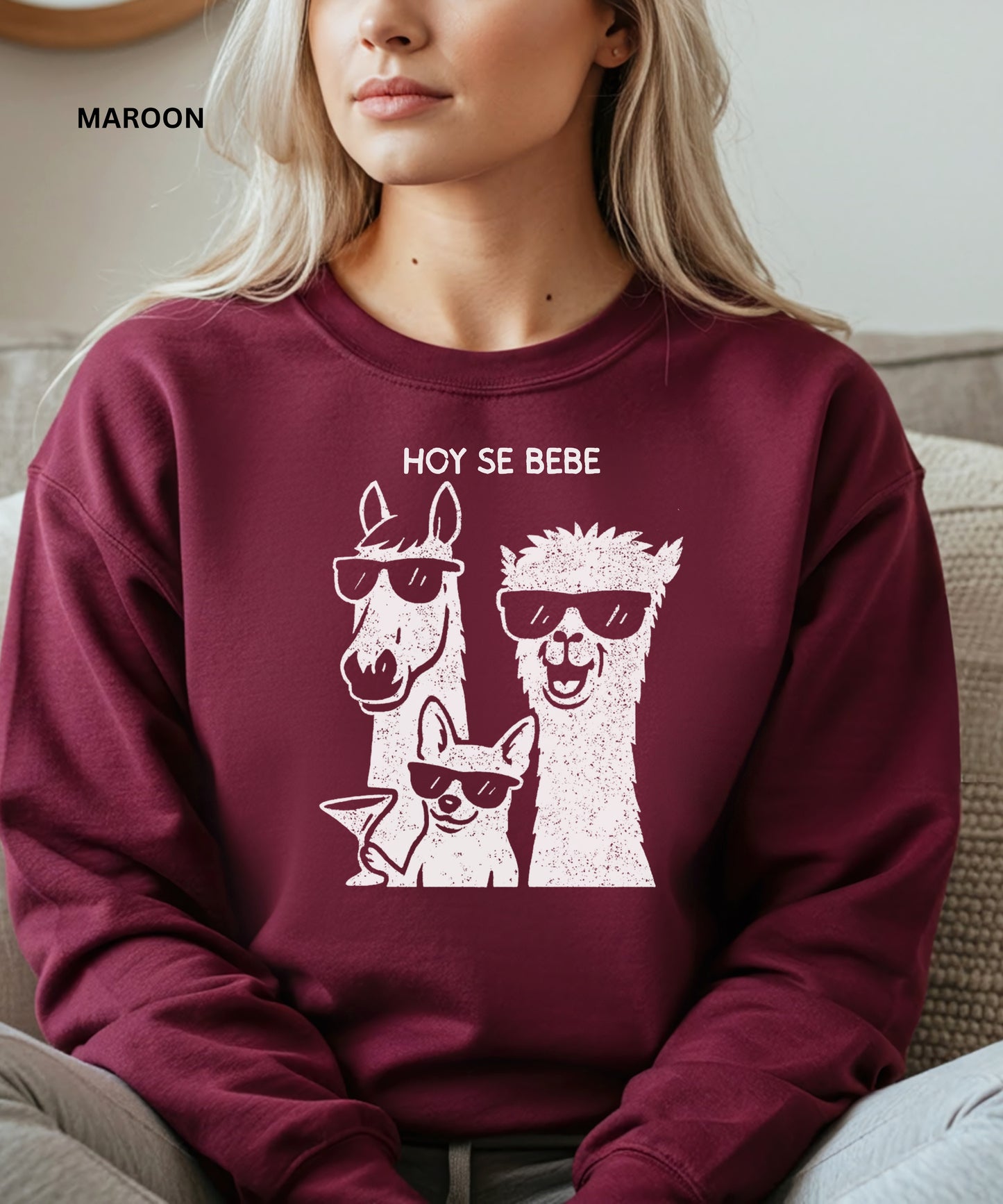 Person wearing a maroon sweatshirt with llama and dog graphic and 'HOY SE BEBE' text.