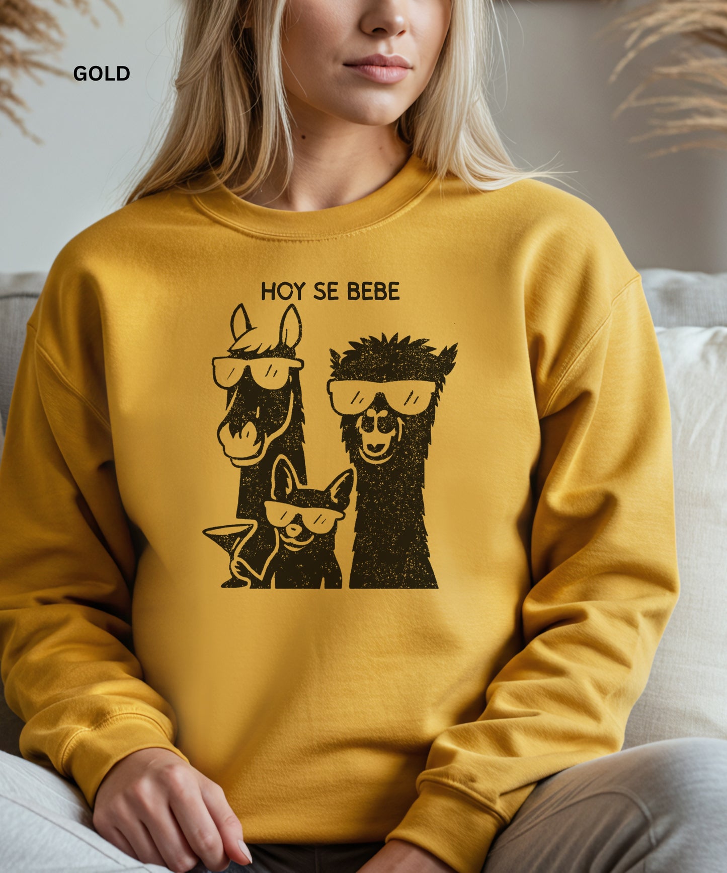Person wearing a gold sweatshirt with llama and dog graphic and 'HOY SE BEBE' text.