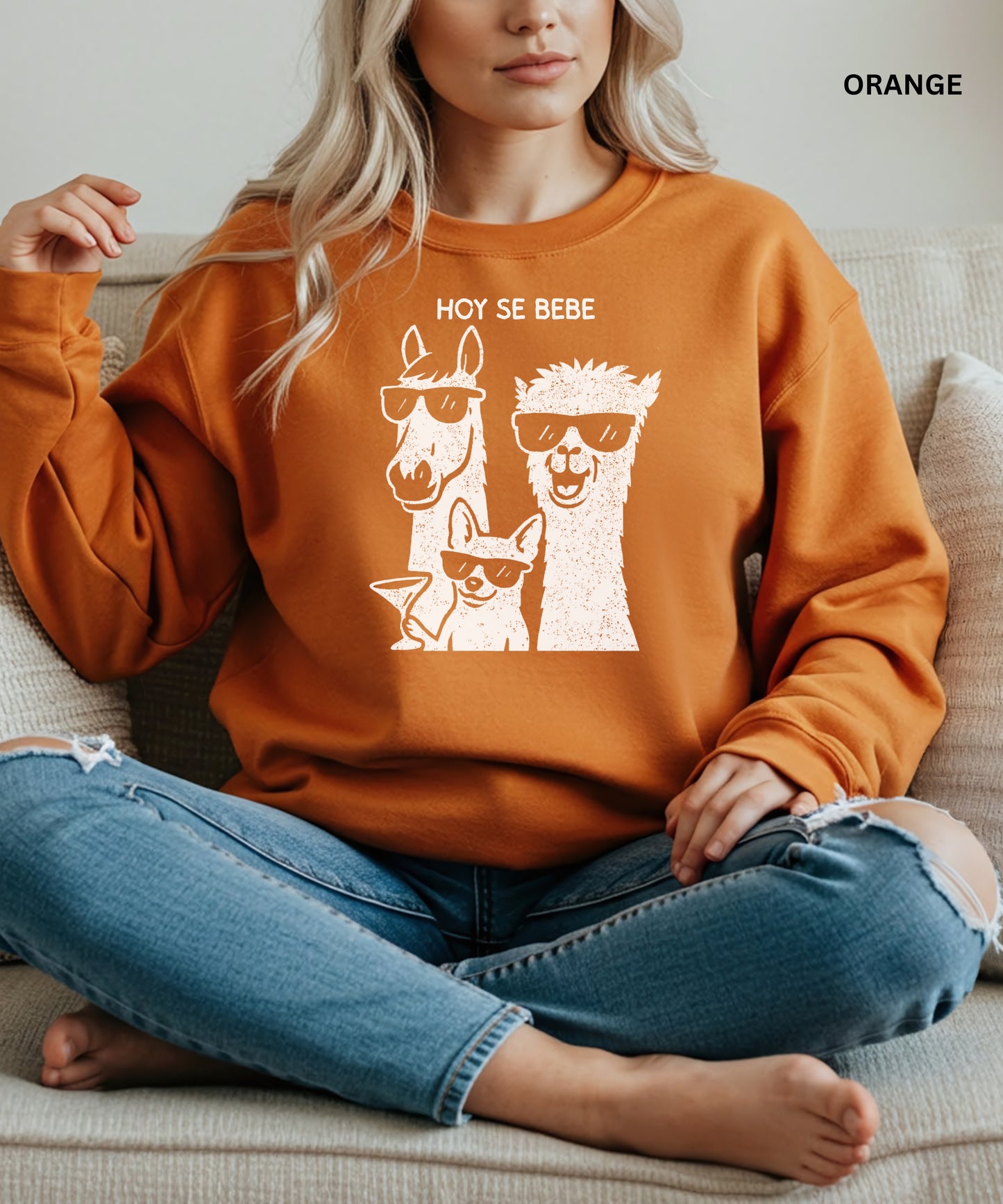 Person wearing an orange sweatshirt with llama and dog graphic and 'HOY SE BEBE' text.