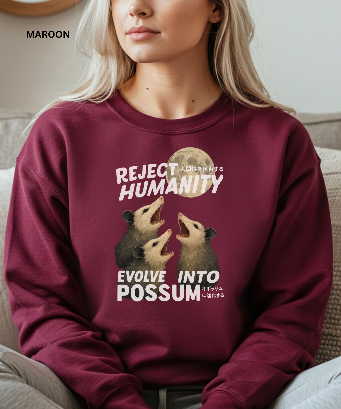 Person wearing a maroon colored sweatshirt with a graphic design that says "reject humanity evolve into possum" sitting on a couch.