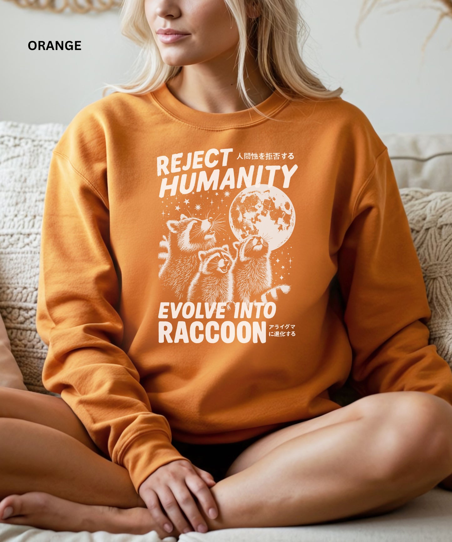 Person wearing an orange colored sweatshirt with a graphic design that says "reject humanity evolve into racoon" sitting on a couch.