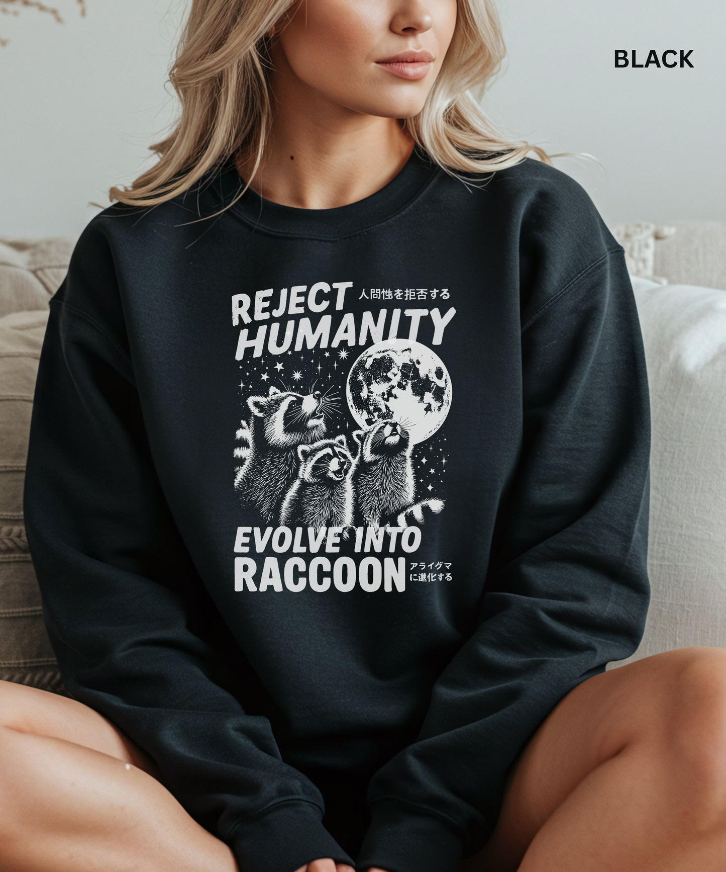 Person wearing a black colored sweatshirt with a graphic design that says "reject humanity evolve into racoon" sitting on a couch.