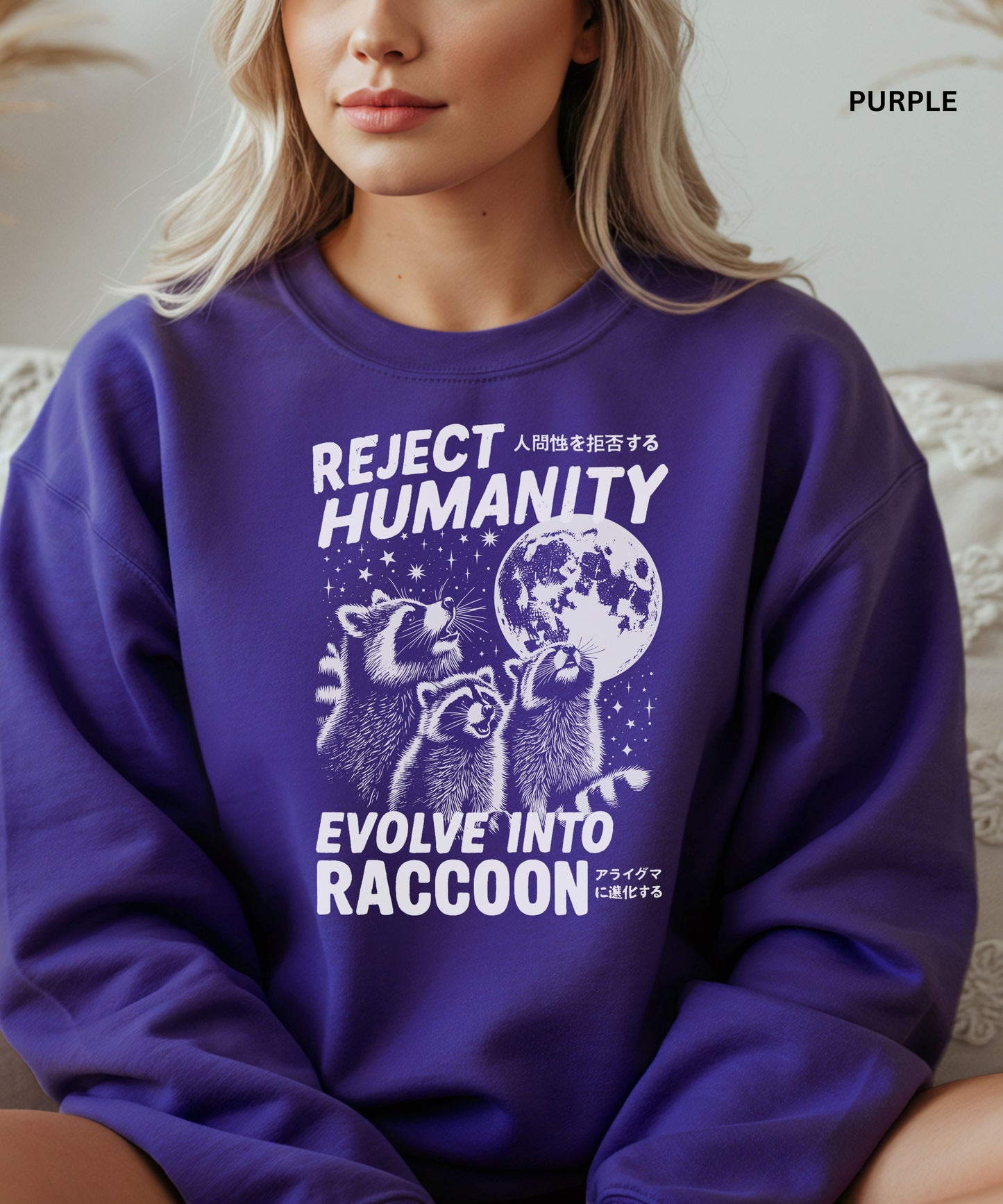 Person wearing a purple colored sweatshirt with a graphic design that says "reject humanity evolve into racoon" sitting on a couch.