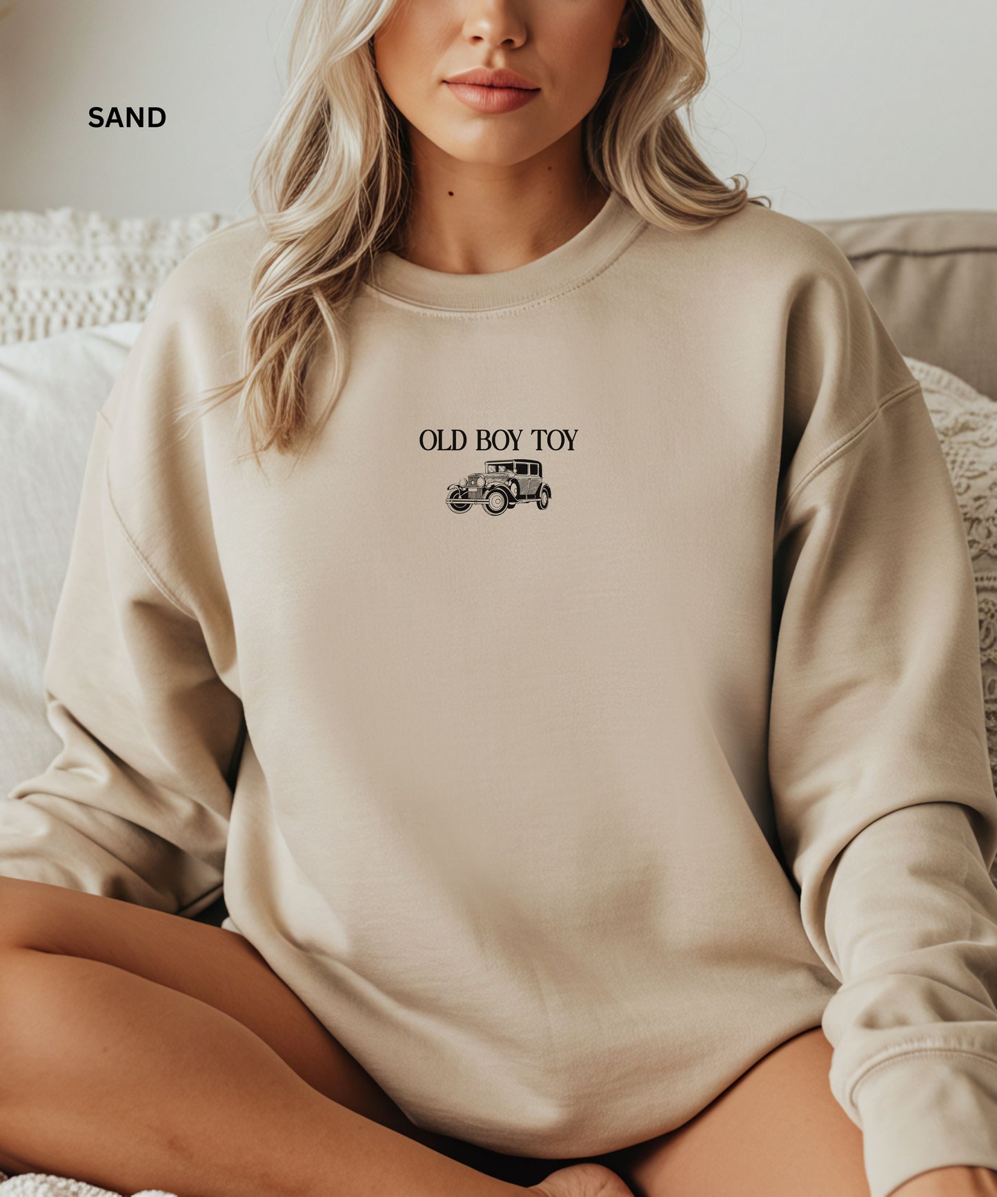 Person wearing a beige sweatshirt with 'Old Boy Toy' text and graphic, sitting on a couch.