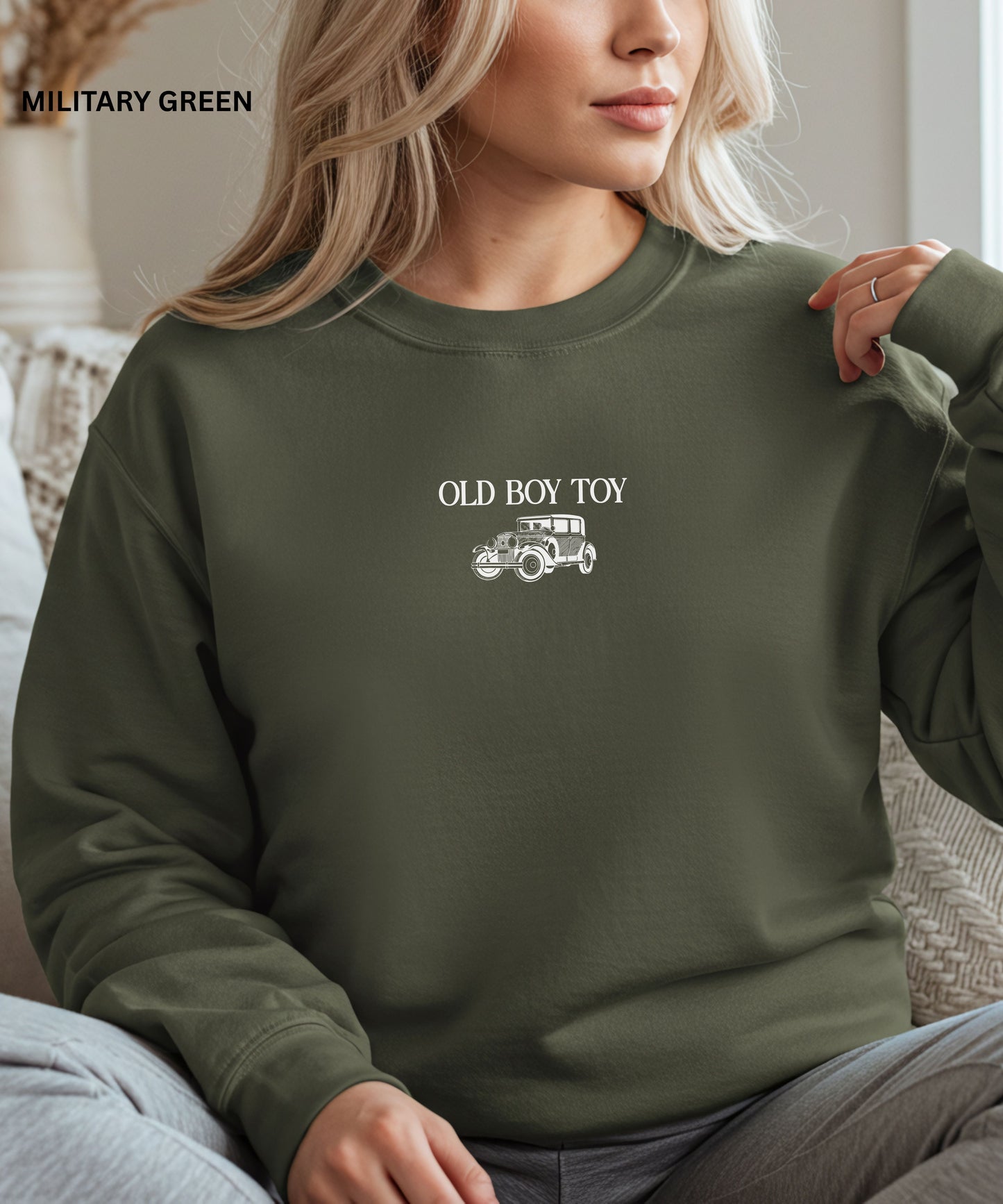 Person wearing a green sweatshirt with 'Old Boy Toy' and car graphic, sitting indoors.