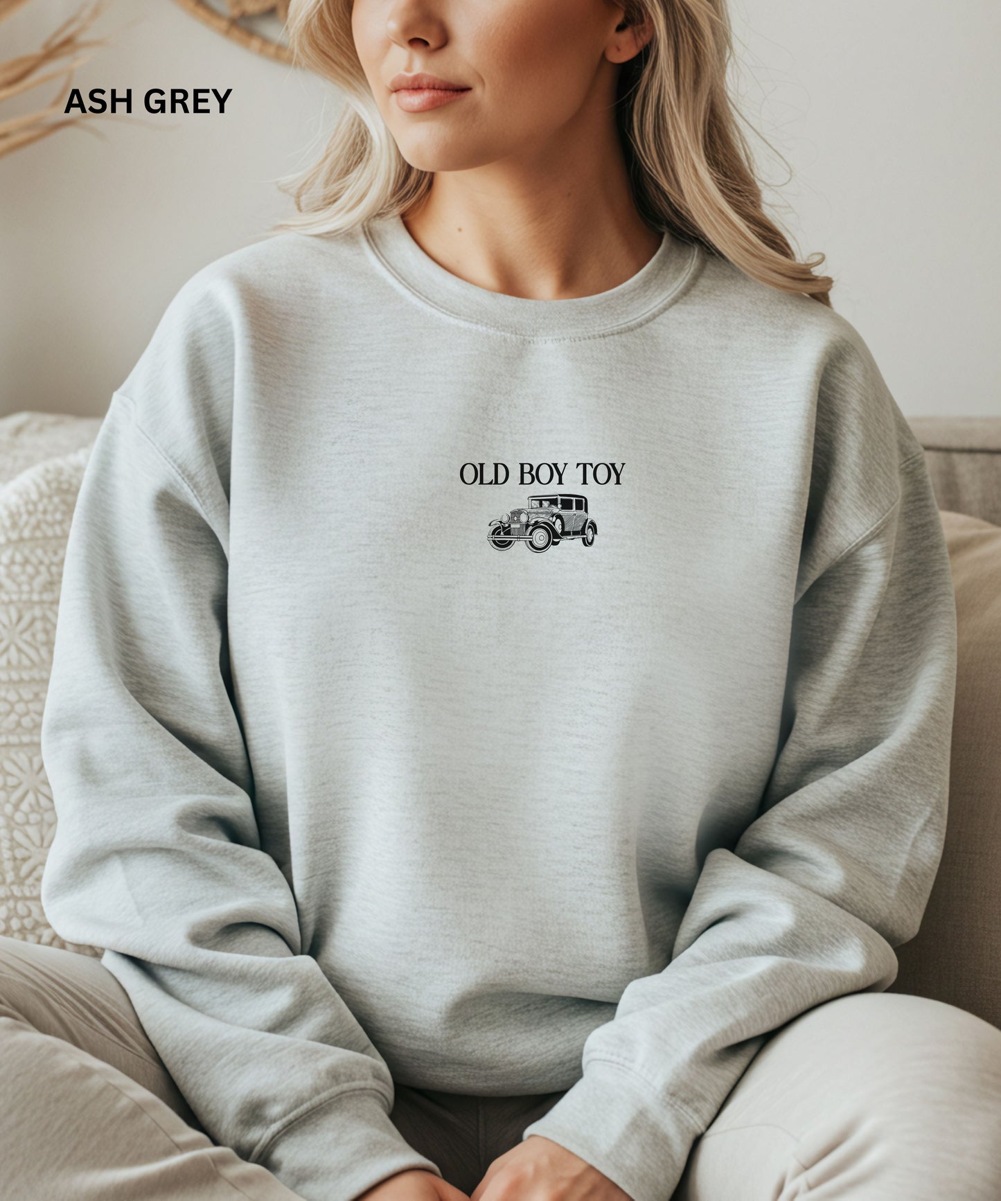 Person wearing an ash grey sweatshirt with 'Old Boy Toy' text and graphic.