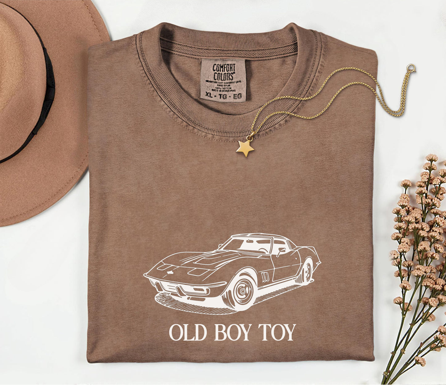 Brown t-shirt with car design and 'Old Boy Toy' text, accompanied by a hat and necklace on a white background.