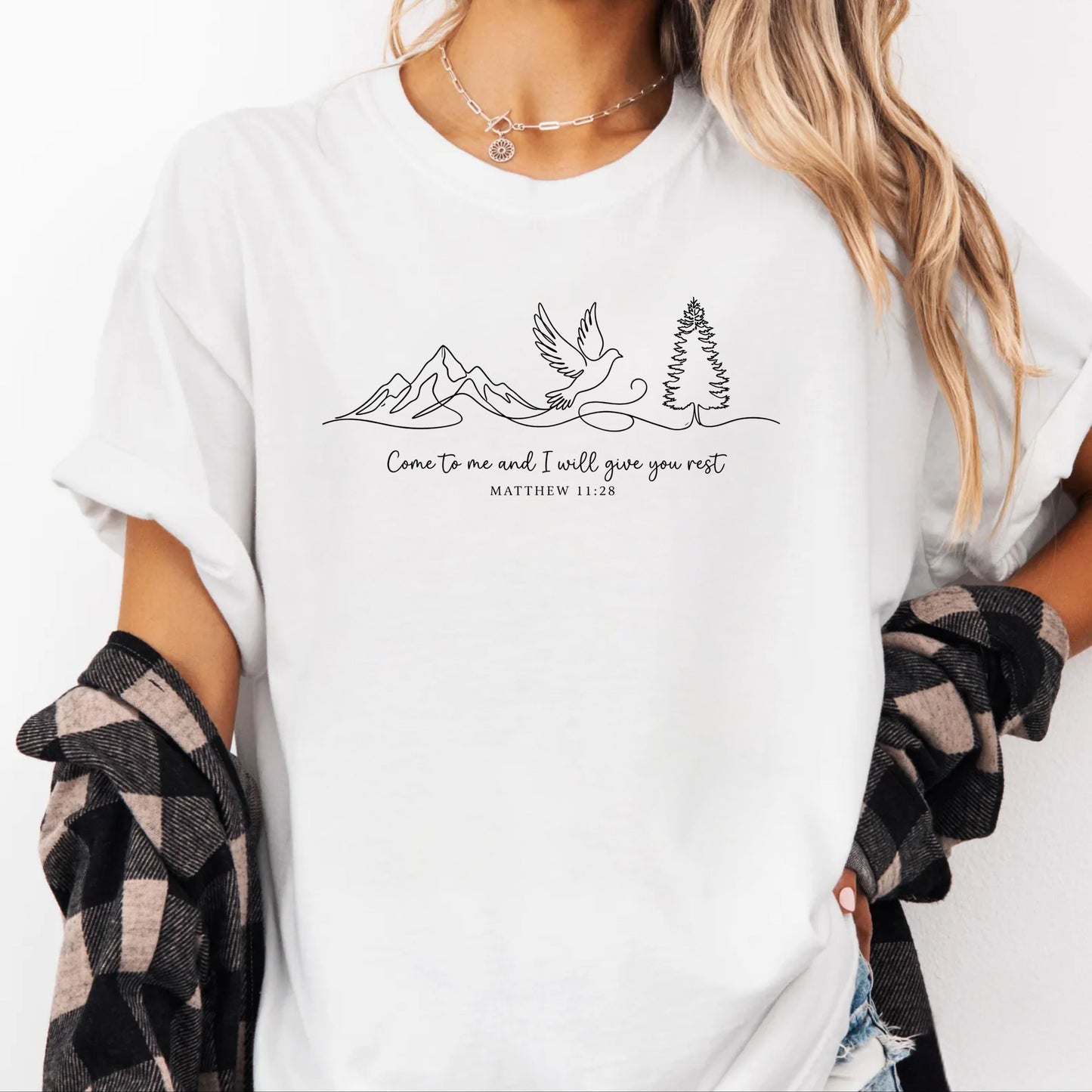 Person wearing a white t-shirt with nature-themed design and text that says "come to me and i will give you rest matthew 11:28" 