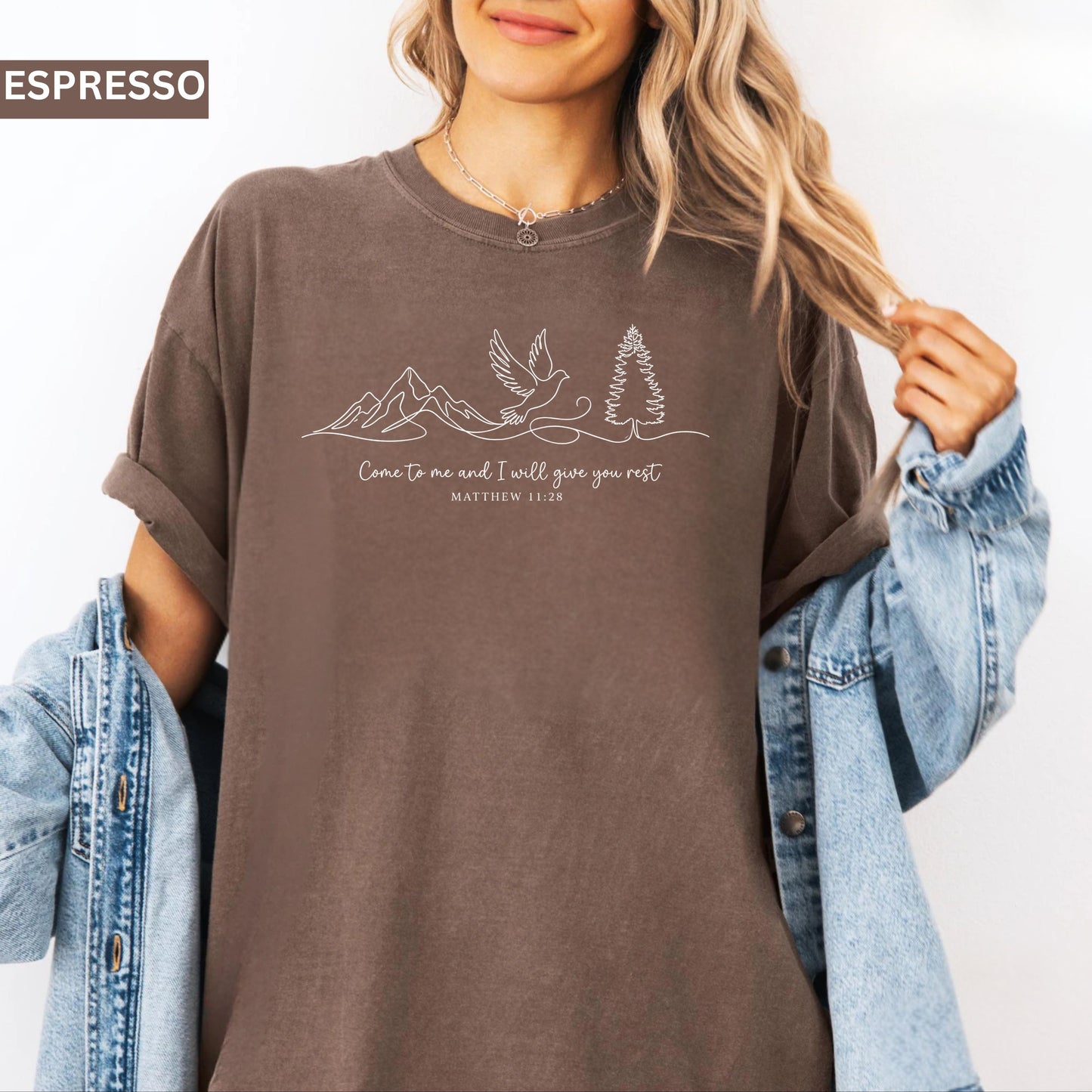 Person wearing an espresso colored t-shirt with nature-themed design and text that says "come to me and i will give you rest matthew 11:28" 