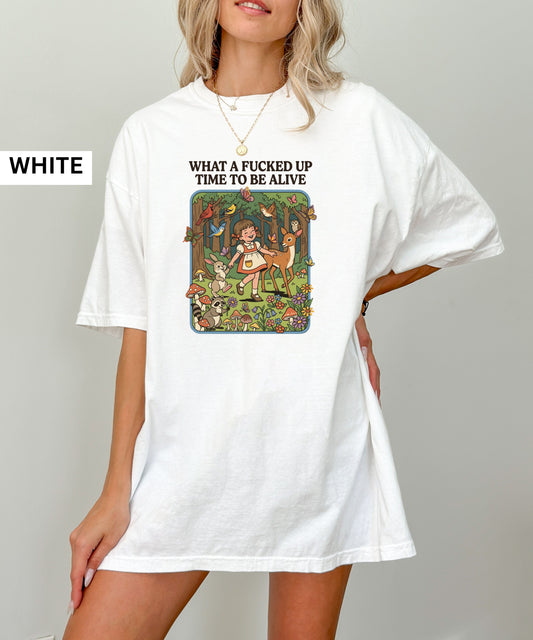 white t-shirt with graphic design and text 'What a fucked up time to be alive' on a white surface.