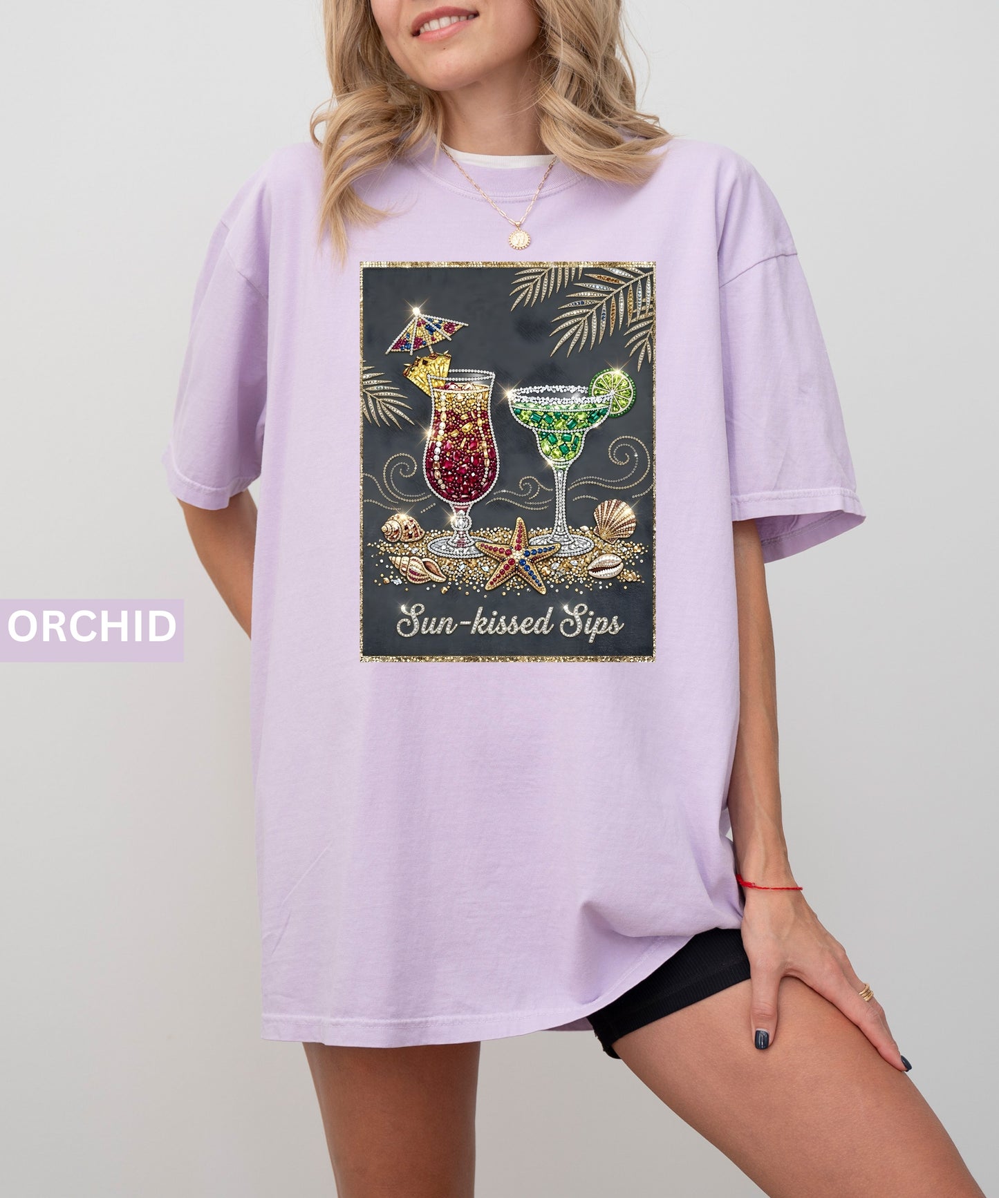 Person wearing an orchid t-shirt with a graphic design of cocktails and text 'Sun-kissed Sips' on a plain background.