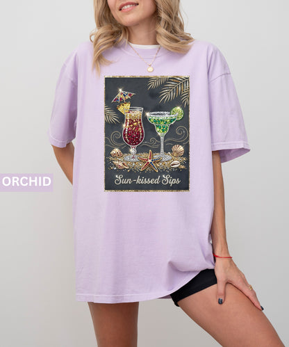Person wearing an orchid t-shirt with a graphic design of cocktails and text 'Sun-kissed Sips' on a plain background.