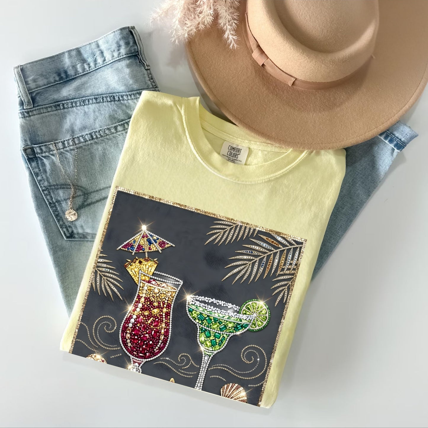 Yellow t-shirt with cocktail design on a white surface with denim jeans and a hat.