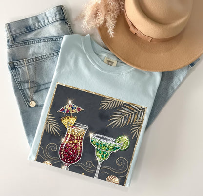 chambray t-shirt with cocktail design, jeans, and hat on a white surface