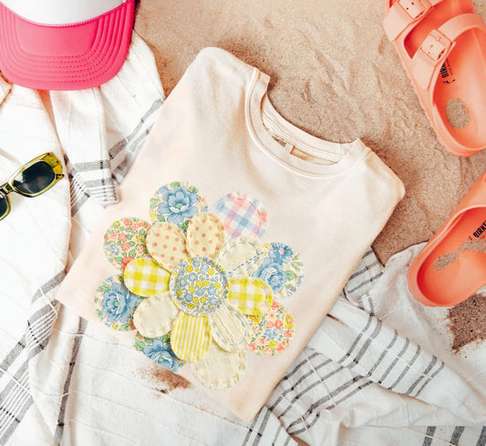 Beige sweatshirt with floral design on a sandy surface with accessories like sunglasses and sandals.