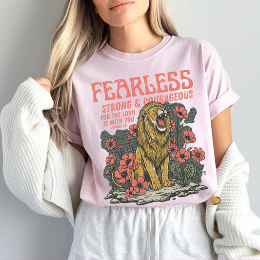 Person wearing a pink t-shirt with a lion graphic and text fearless strong and courageous, against a plain background