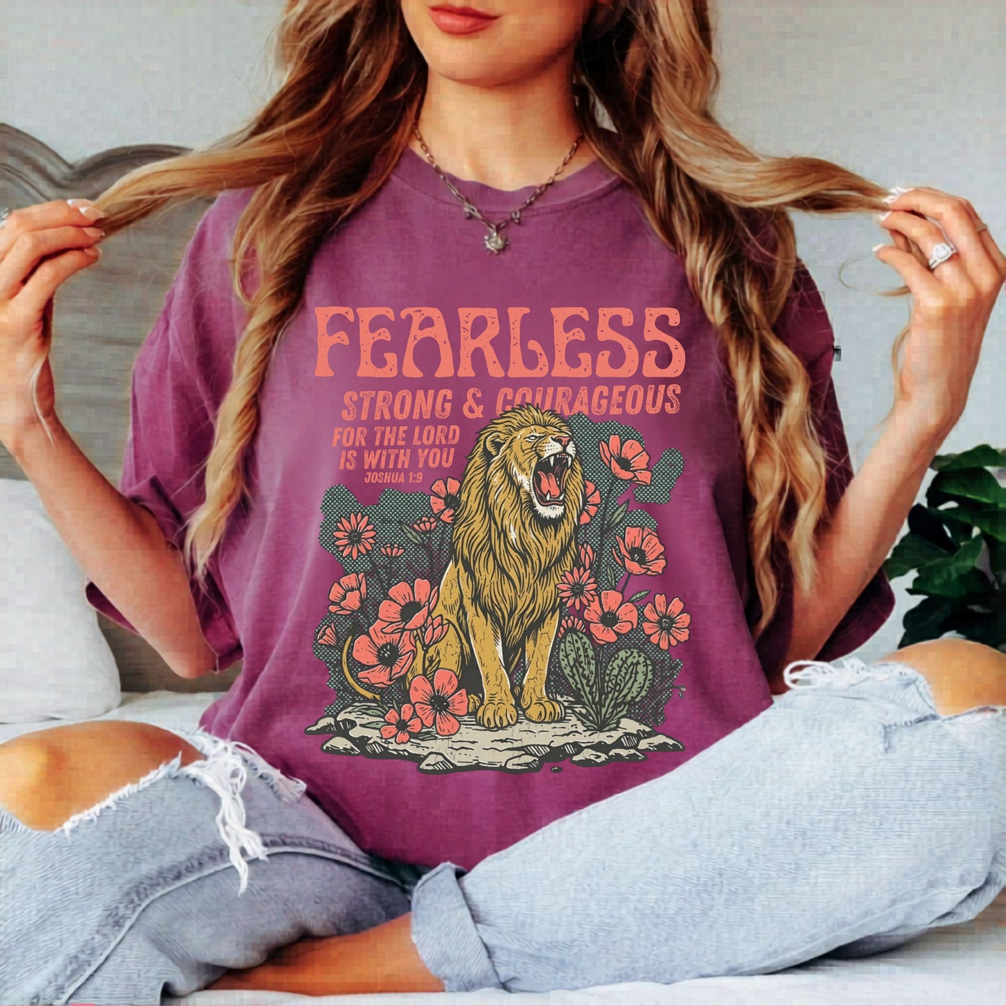 Person wearing a berry colored t-shirt with a lion graphic and text fearless strong and courageous, against a plain background