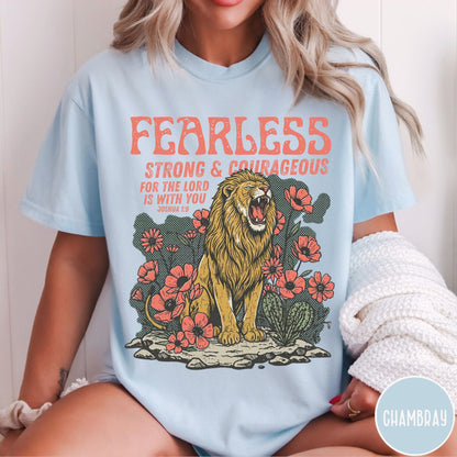 Person wearing a light blue t-shirt with a lion graphic and text fearless strong and courageous, sitting against a white background.
