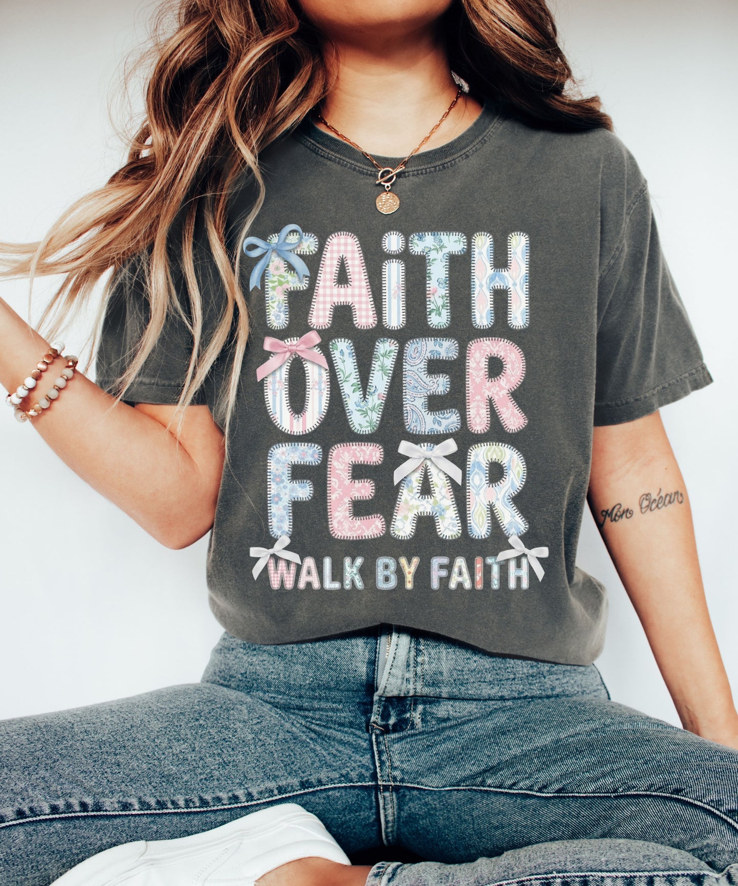 Person wearing a pepper color t-shirt with 'Faith Over Fear' text design.