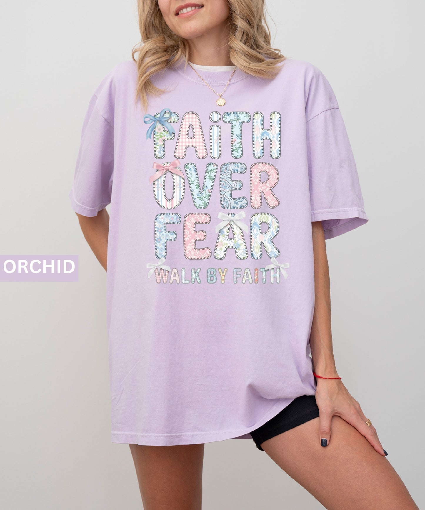 Person wearing an orchid colored  t-shirt with 'Faith Over Fear' text on a plain background