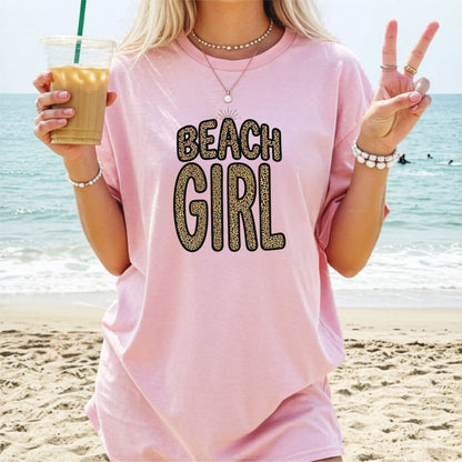 Person wearing a blossom 'Beach Girl' shirt on a beach, holding a drink.